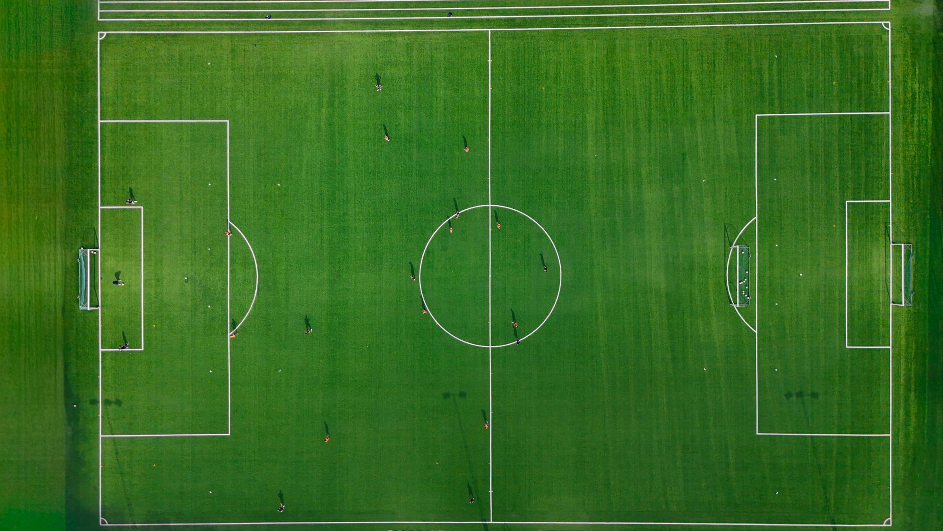 a professional football practice field at a training facility, with blocking sleds, orange cones, and yard-line markings visible under clear summer sky, no players as focal point