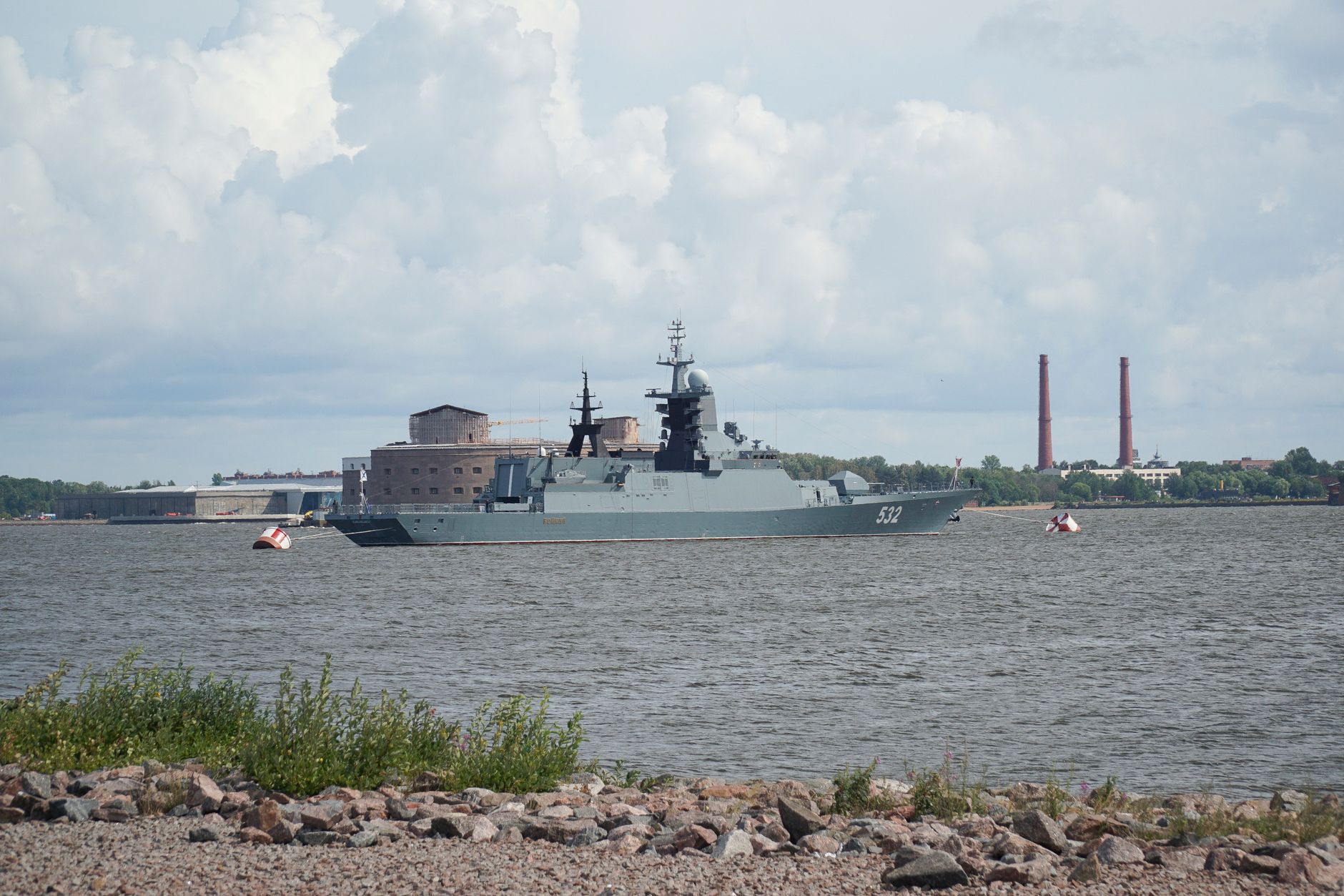a Tomahawk missile being loaded onto a U.S. Navy surface combatant at a naval pier, the ship's vertical launch system cells open and visible in the foreground
