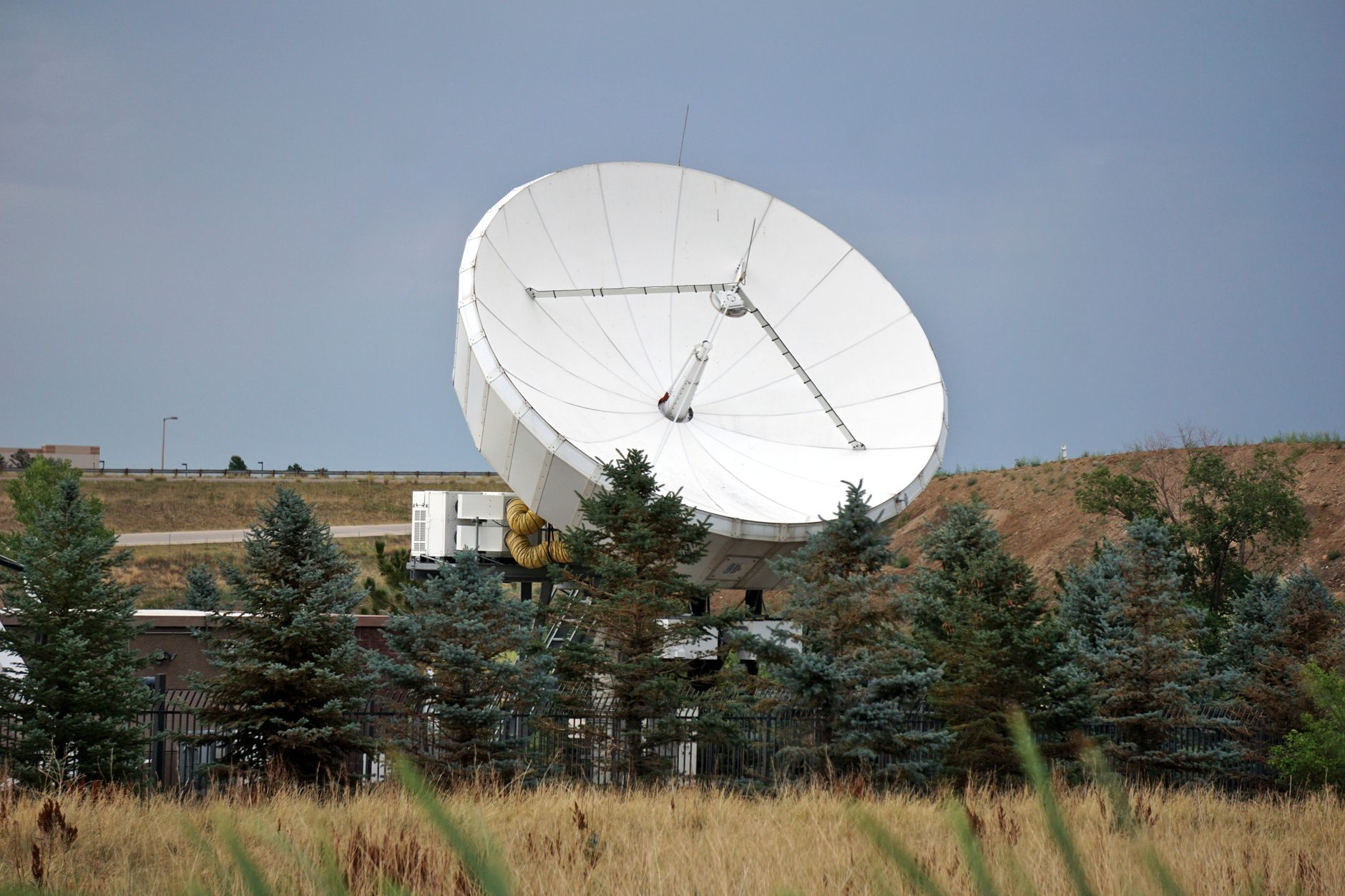 a ground-based radar installation with large rotating dish antenna at a military air-defense site, surrounded by trees and antenna support equipment