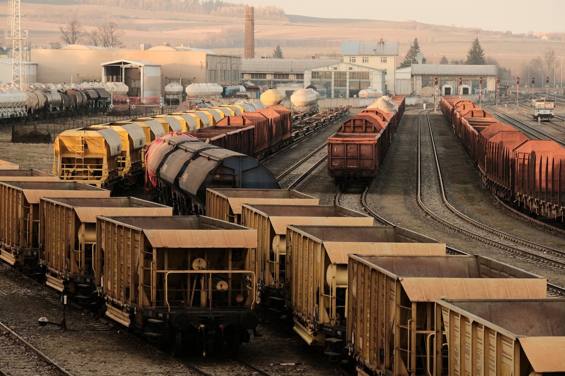 a rail freight yard with cargo containers and industrial cranes along a wide track corridor, overcast sky, no personnel in foreground