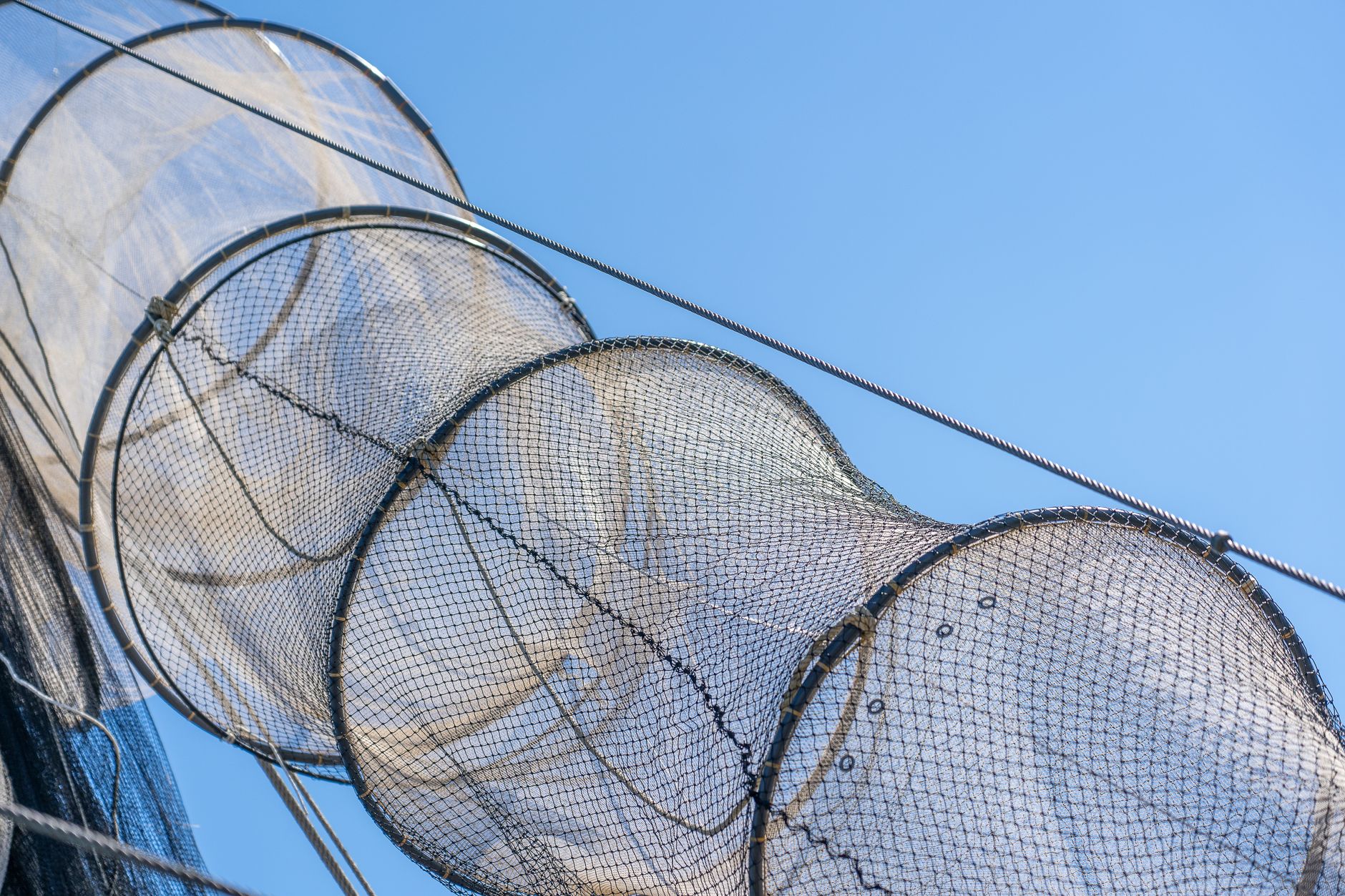 close-up view of heavy steel-mesh anti-torpedo netting suspended from floating buoys alongside a submarine pier at a cold-weather naval installation, with gray Arctic water visible beneath