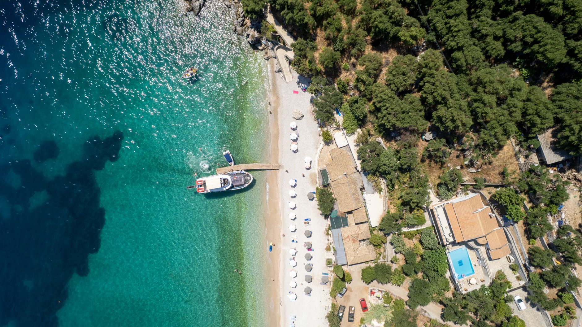 aerial view of a small naval facility with modest pier infrastructure and berthed support vessels along a Mediterranean coastline