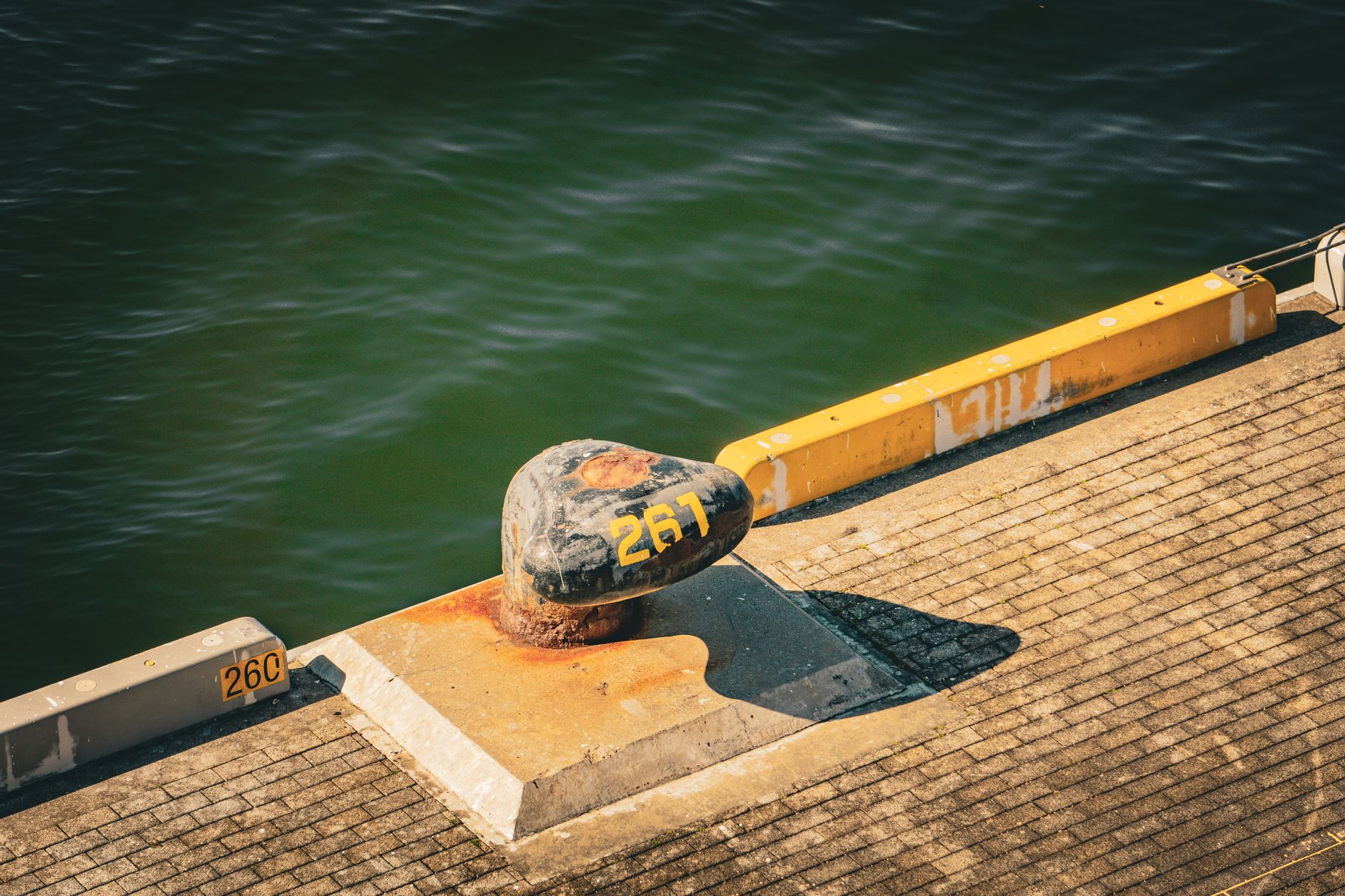 a mostly empty naval pier with rusting bollards and shallow-draft berthing infrastructure along a coastal facility, with calm sea in the background