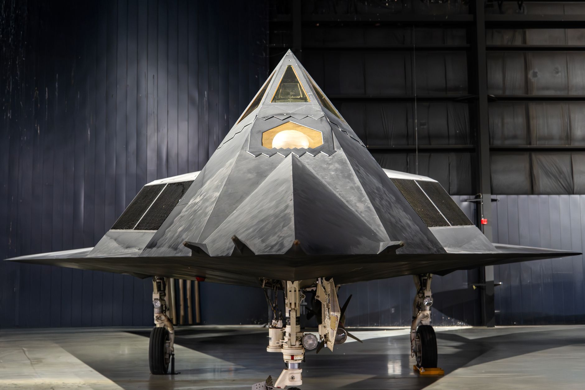 a scale model of a delta-wing stealth drone concept displayed on a white exhibition stand at an aerospace trade show, viewed from a three-quarter front angle