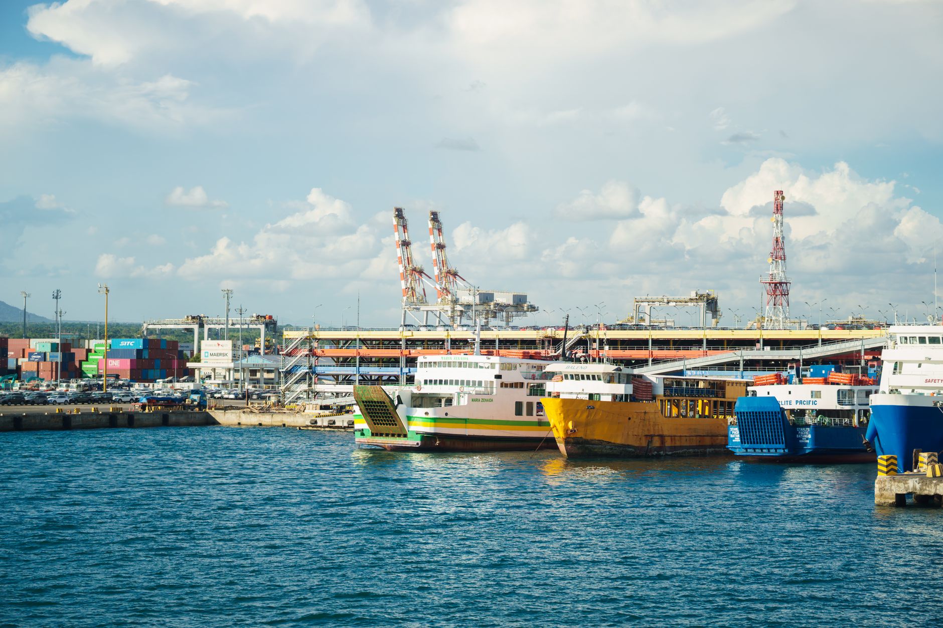 a cluster of compact unmanned surface vessels moored at a small coastal pier, with maritime equipment and shoreline infrastructure visible in the background