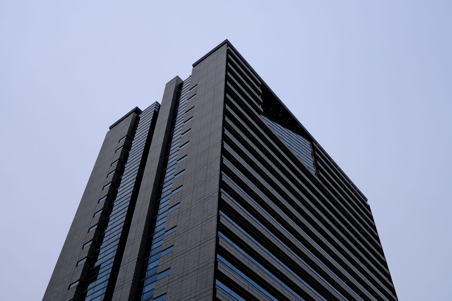 a modern high-rise corporate office tower exterior in Tokyo at dusk, glass facades reflecting city lights, no signage visible