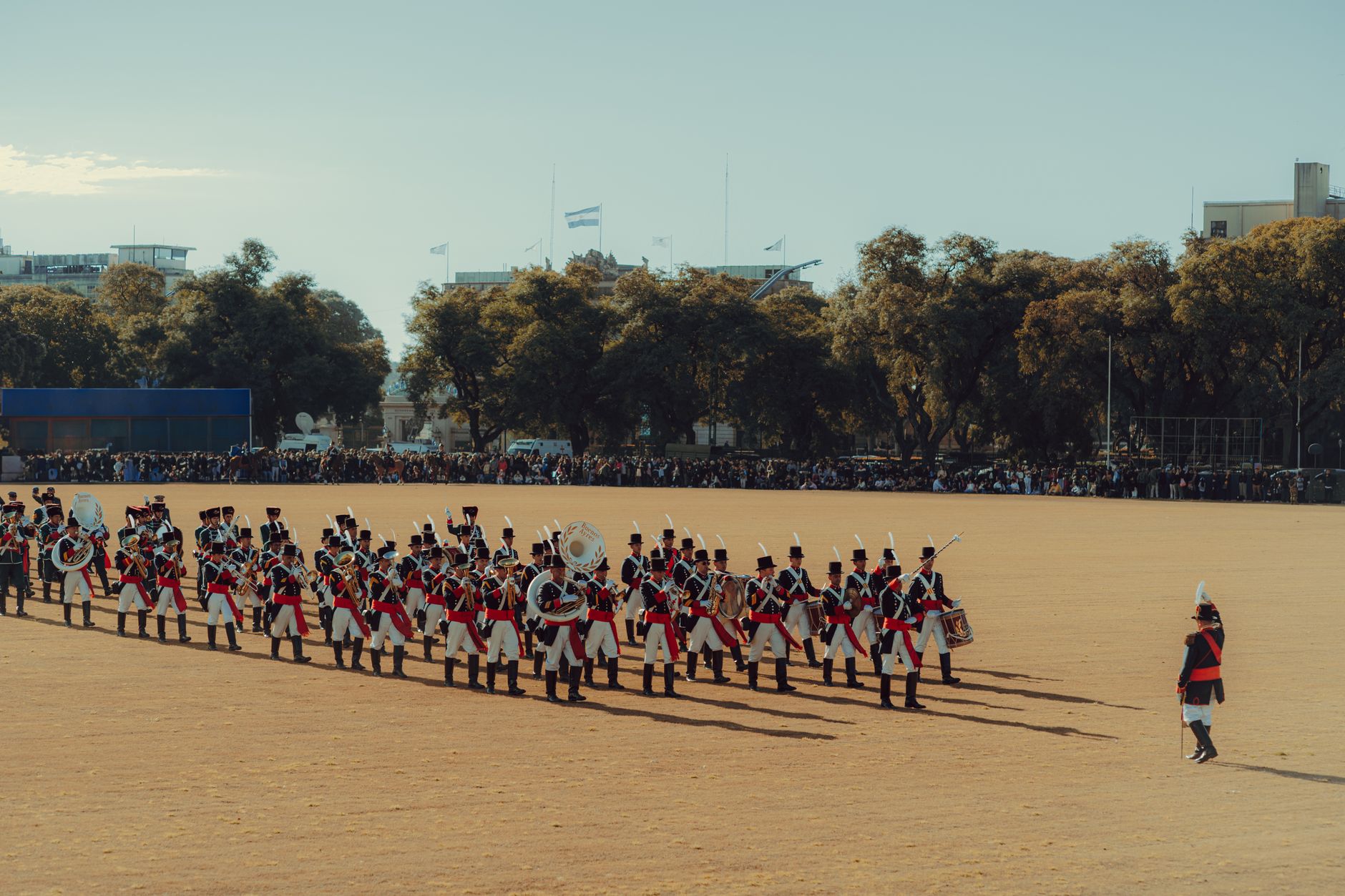 an empty formal military parade ground at dusk with institutional buildings in the background and ornamental flagpoles in the foreground