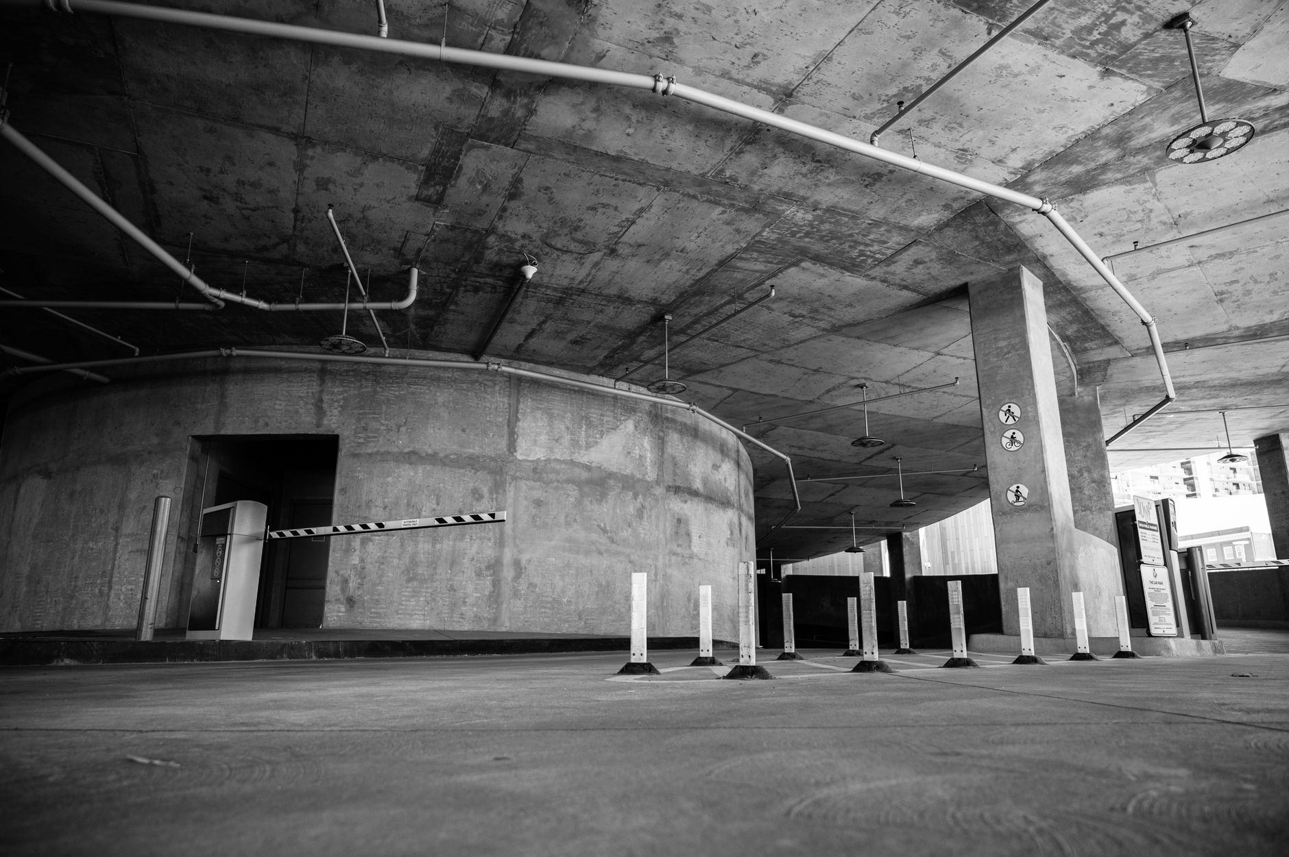 an M1A2 Abrams main battle tank positioned inside a multi-level concrete parking structure, viewed from a low angle showing the vehicle's tracks and hull against bare cement columns