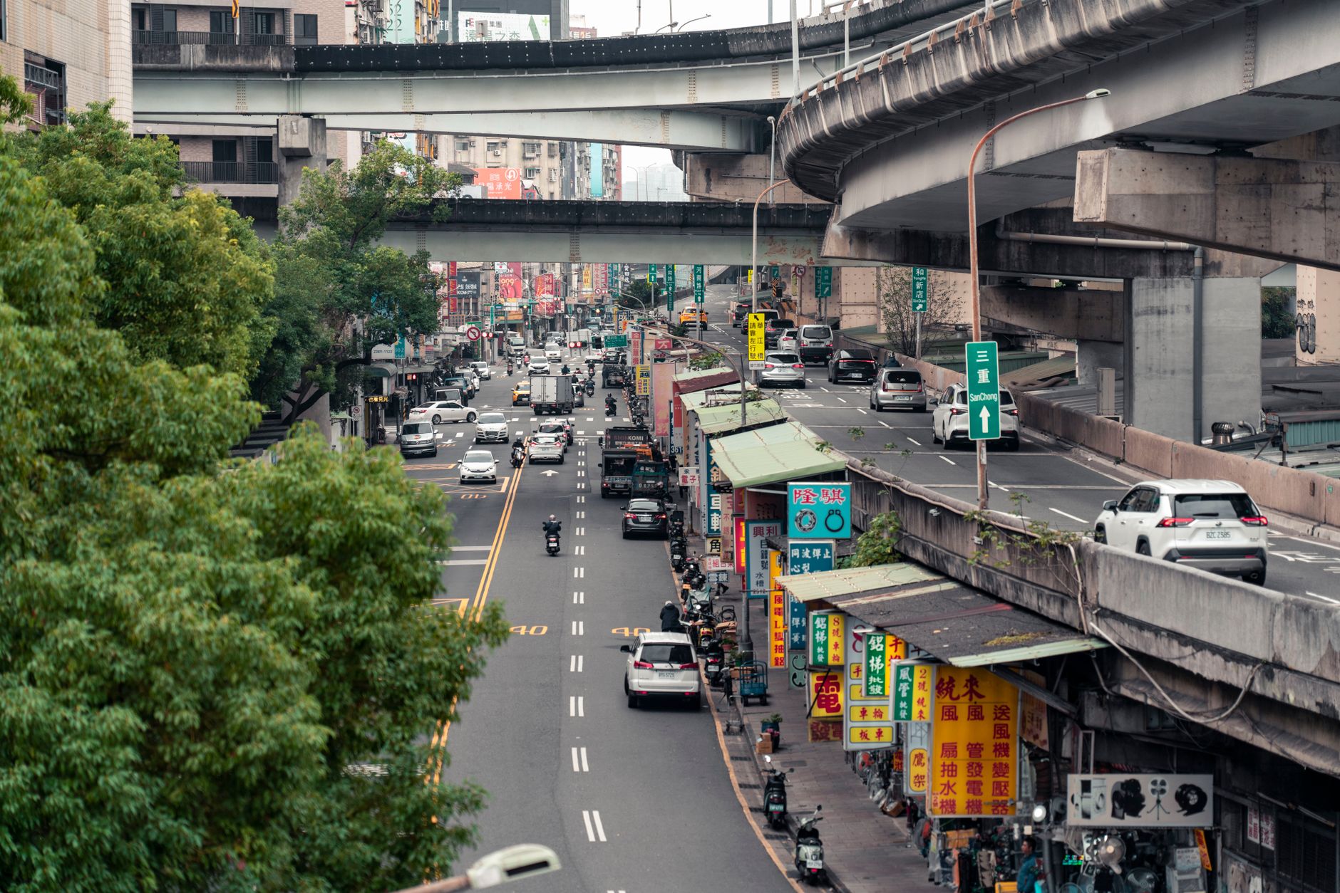 a wide-angle view of a dense Taiwanese urban street scene with elevated highway infrastructure overhead, shot from ground level showing layered concrete overpasses and adjacent commercial buildings
