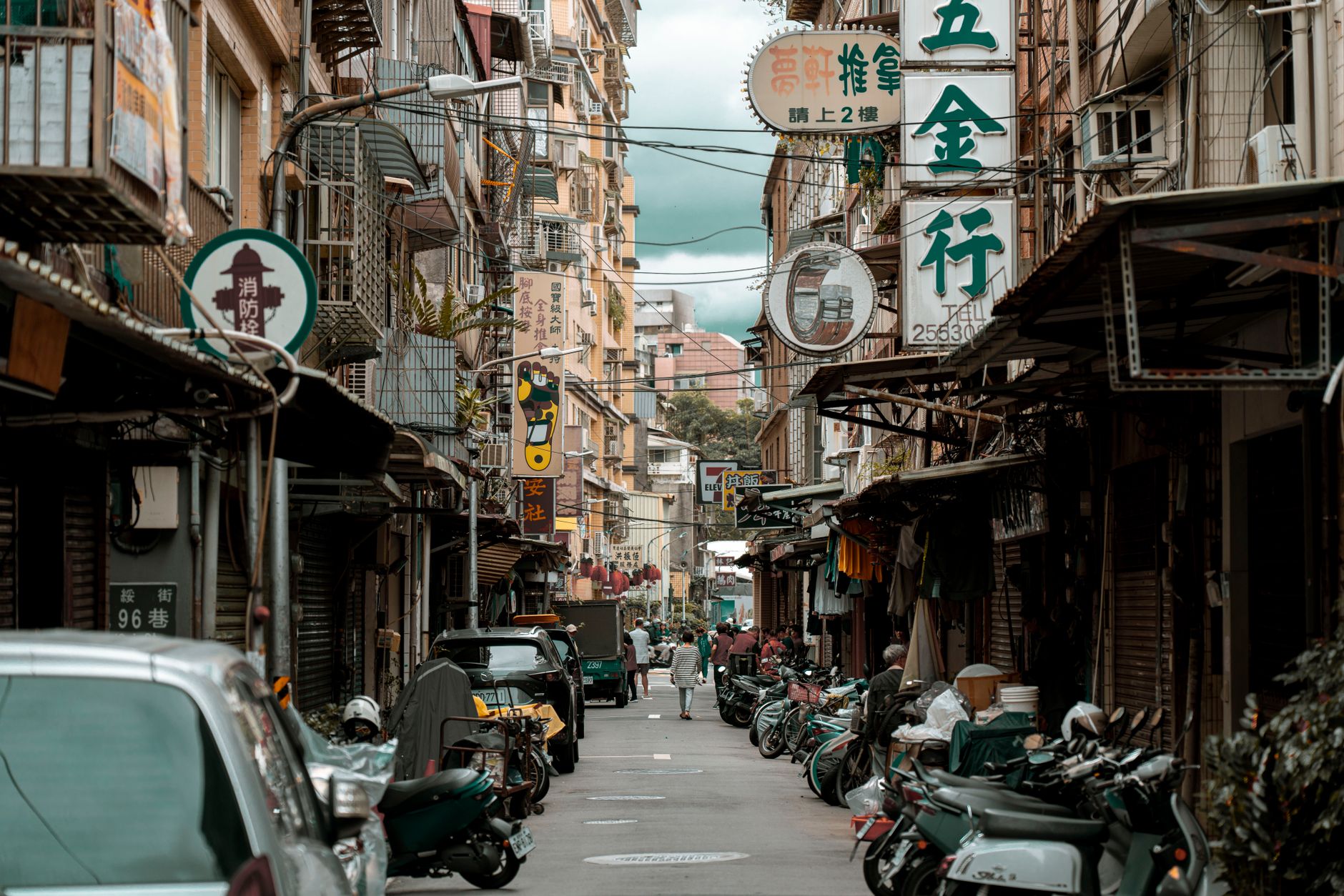 a narrow urban street lined with low-rise apartment buildings and small shops, with military vehicles parked along the curb and soldiers in full kit taking positions near building entrances