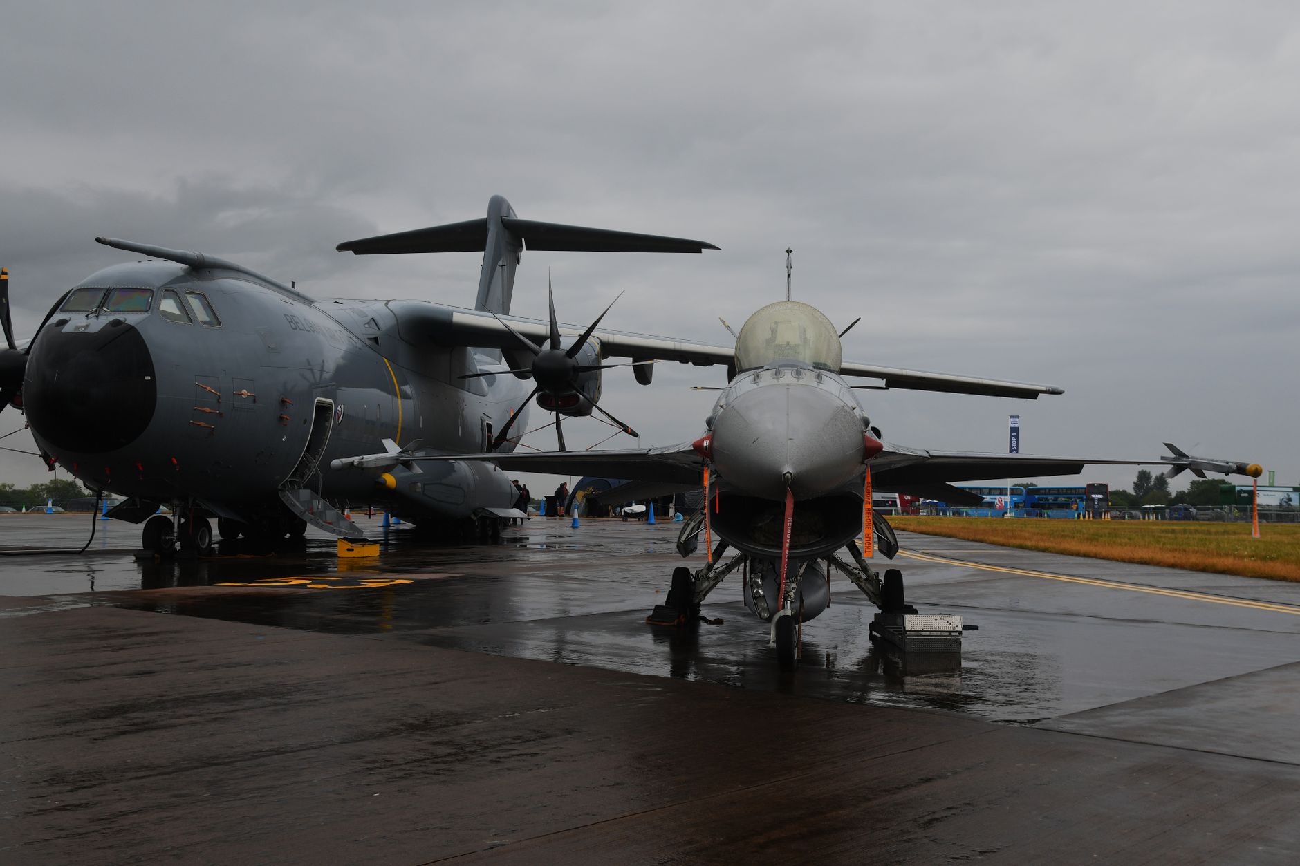 wide interior shot of a large aerospace exhibition hall with military aircraft on static display and exhibition booths, taken from an elevated angle