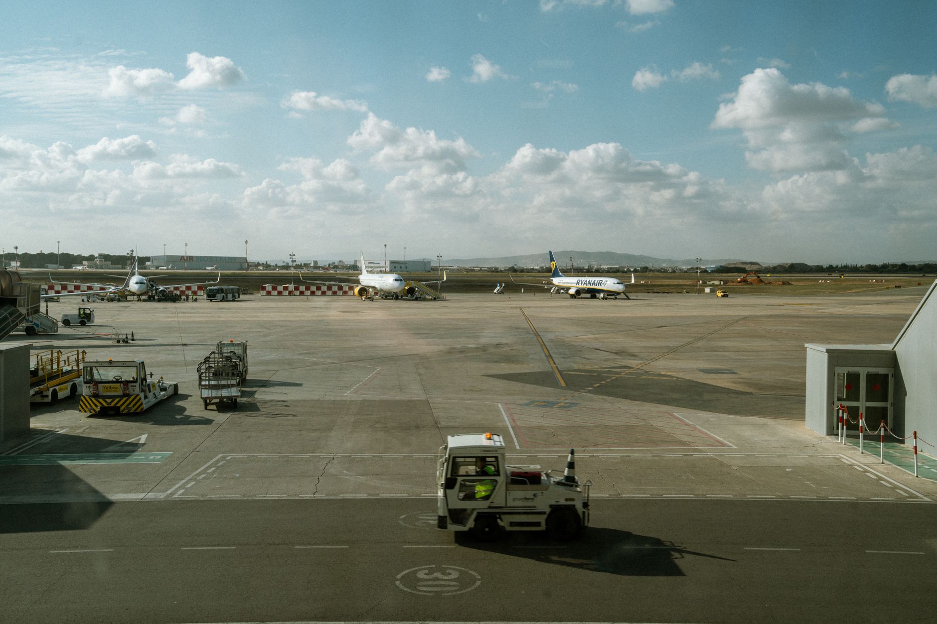 an outdoor airfield apron with a line of ground crew vehicles and communications equipment visible in the foreground, open sky and hangars in the background