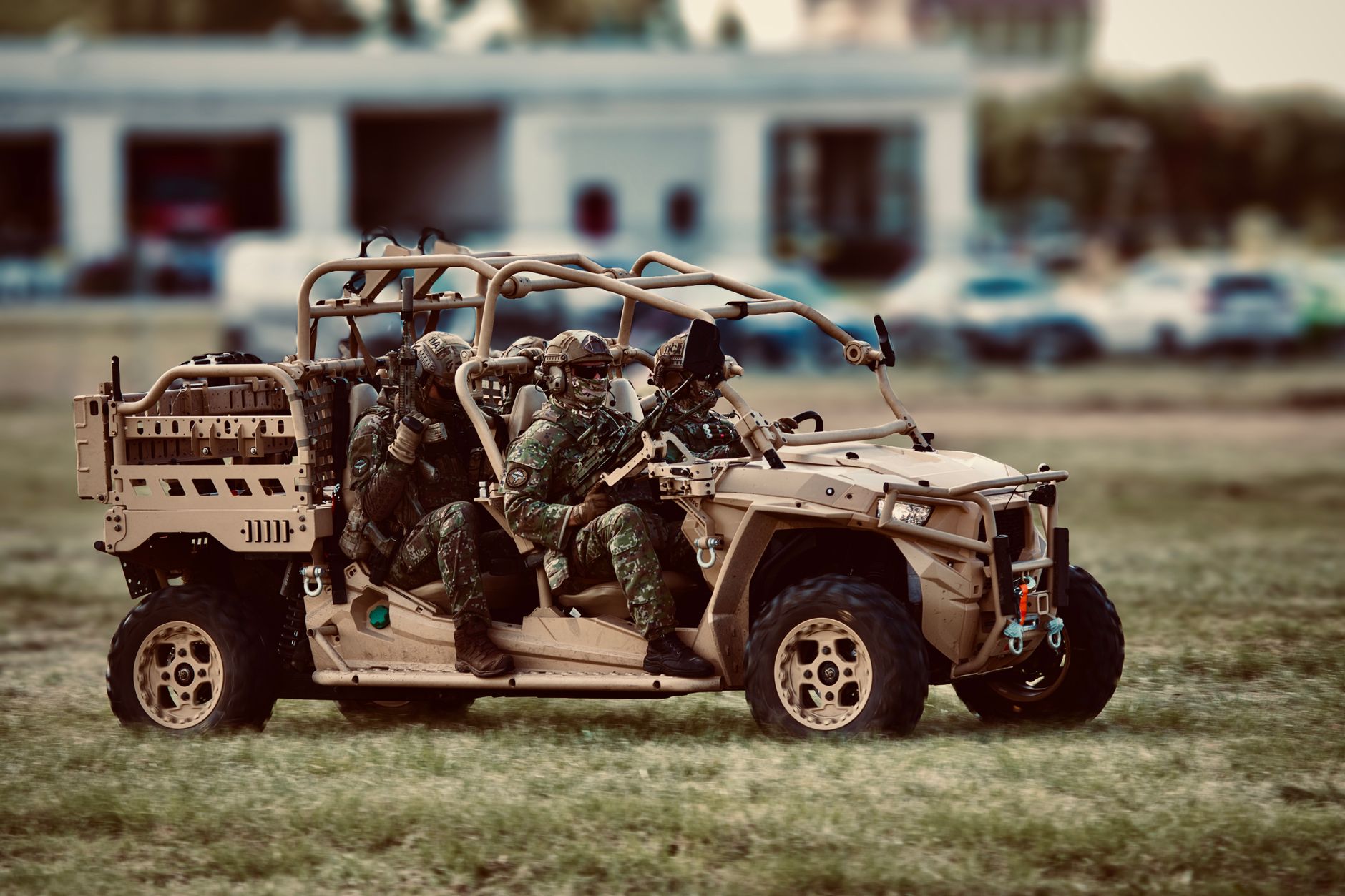 a small tracked unmanned ground vehicle on a dirt training lane at a military base, with sparse woodland in the background and no personnel in frame