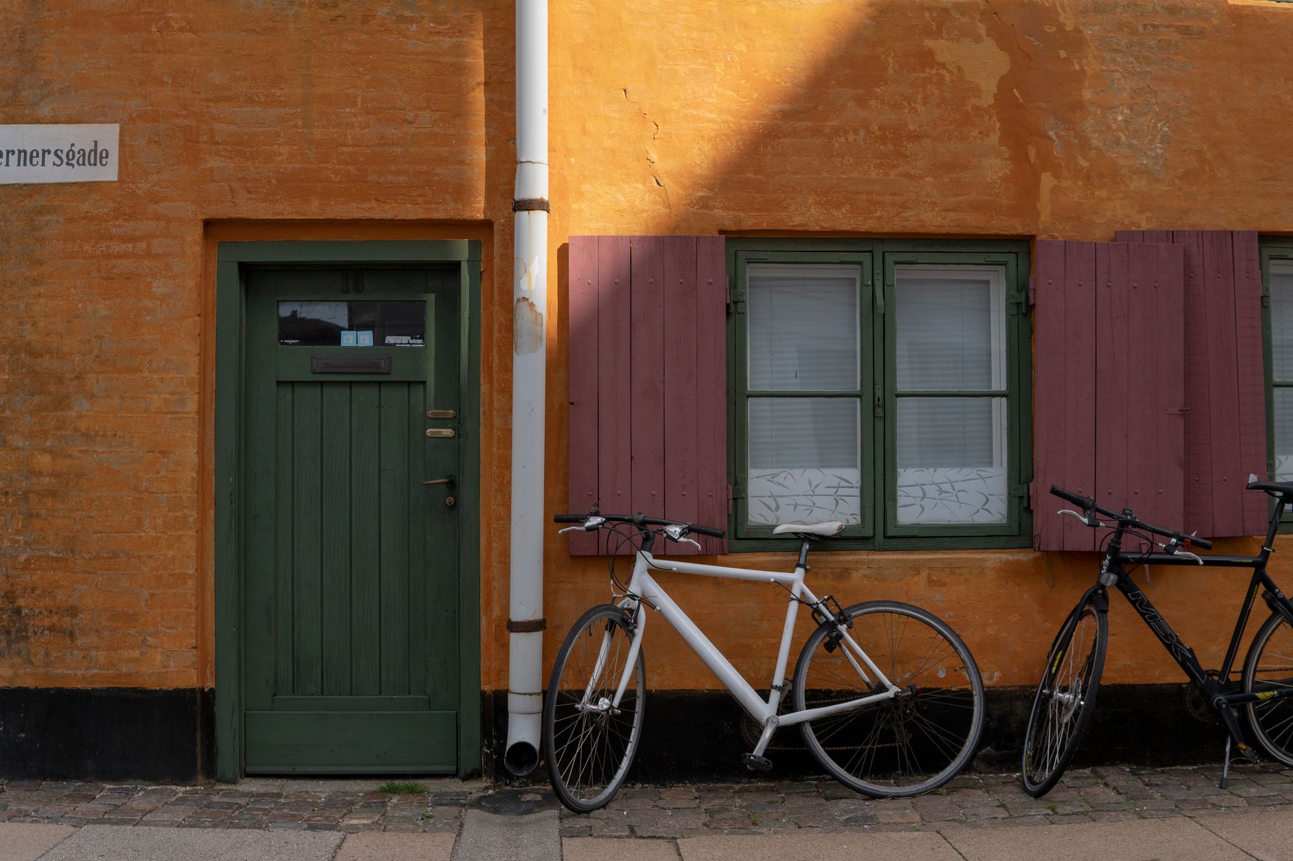a university building facade in a Central European architectural style, windows lit at dusk, a bicycle leaning against a stone wall in the foreground, empty street visible beyond