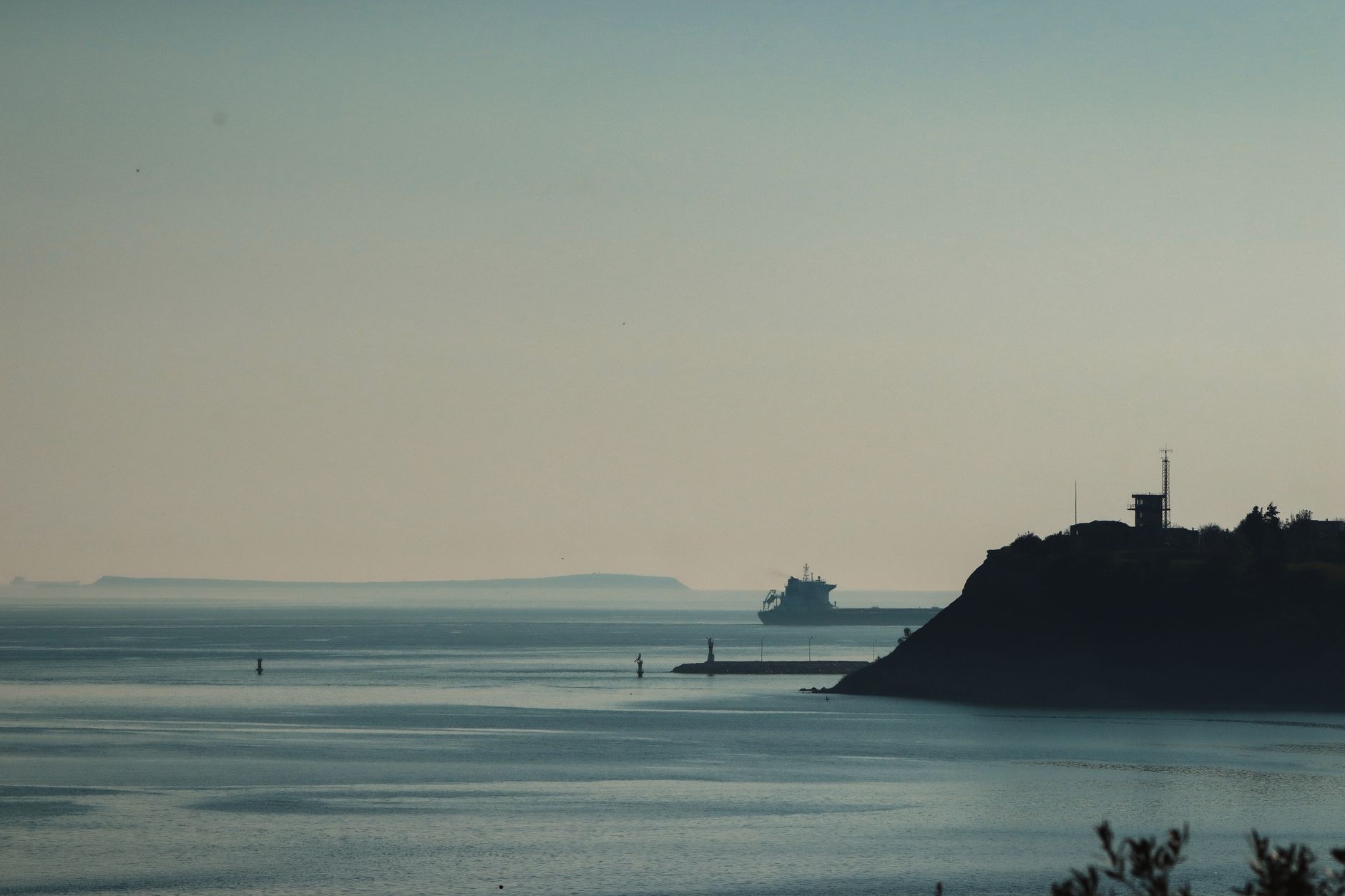 a Nimitz-class aircraft carrier anchored in a calm Pacific harbor, surrounded by escort vessels, viewed from an elevated shoreside vantage point