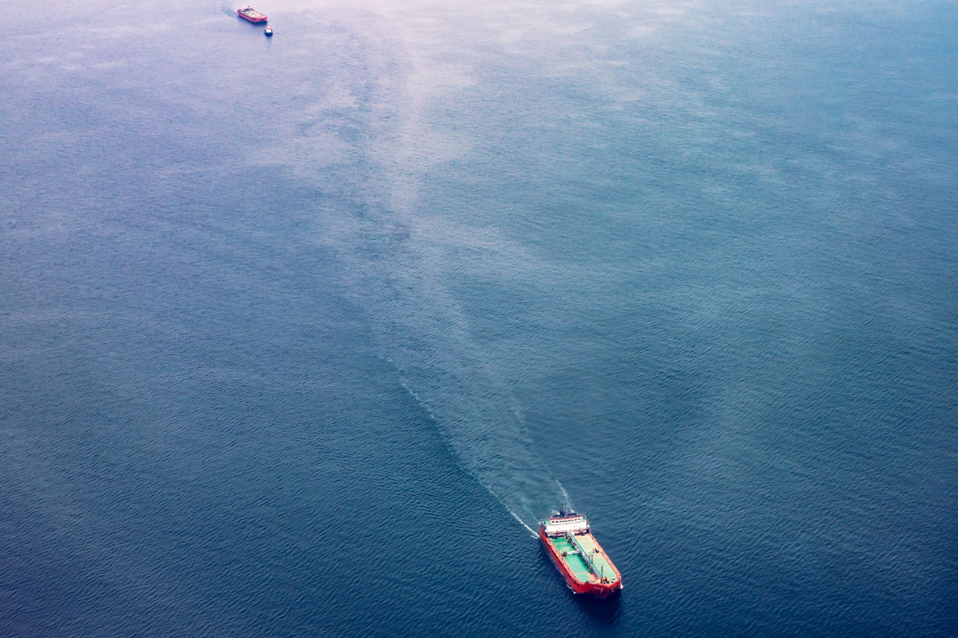 an aerial view of a naval vessel's wake cutting through the narrow blue channel of the Taiwan Strait, with distant coastal geography visible on both horizons
