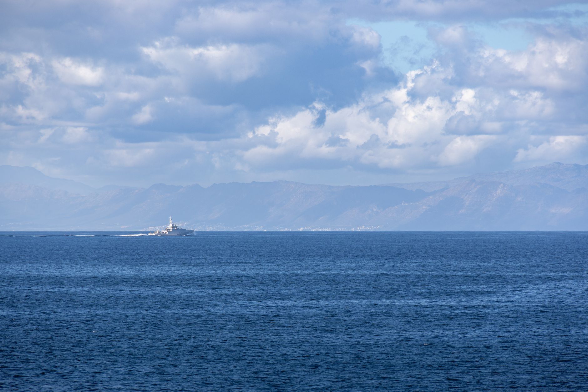 an Arleigh Burke-class guided-missile destroyer viewed from the waterline, at sea in open blue water, with no visible land in the background