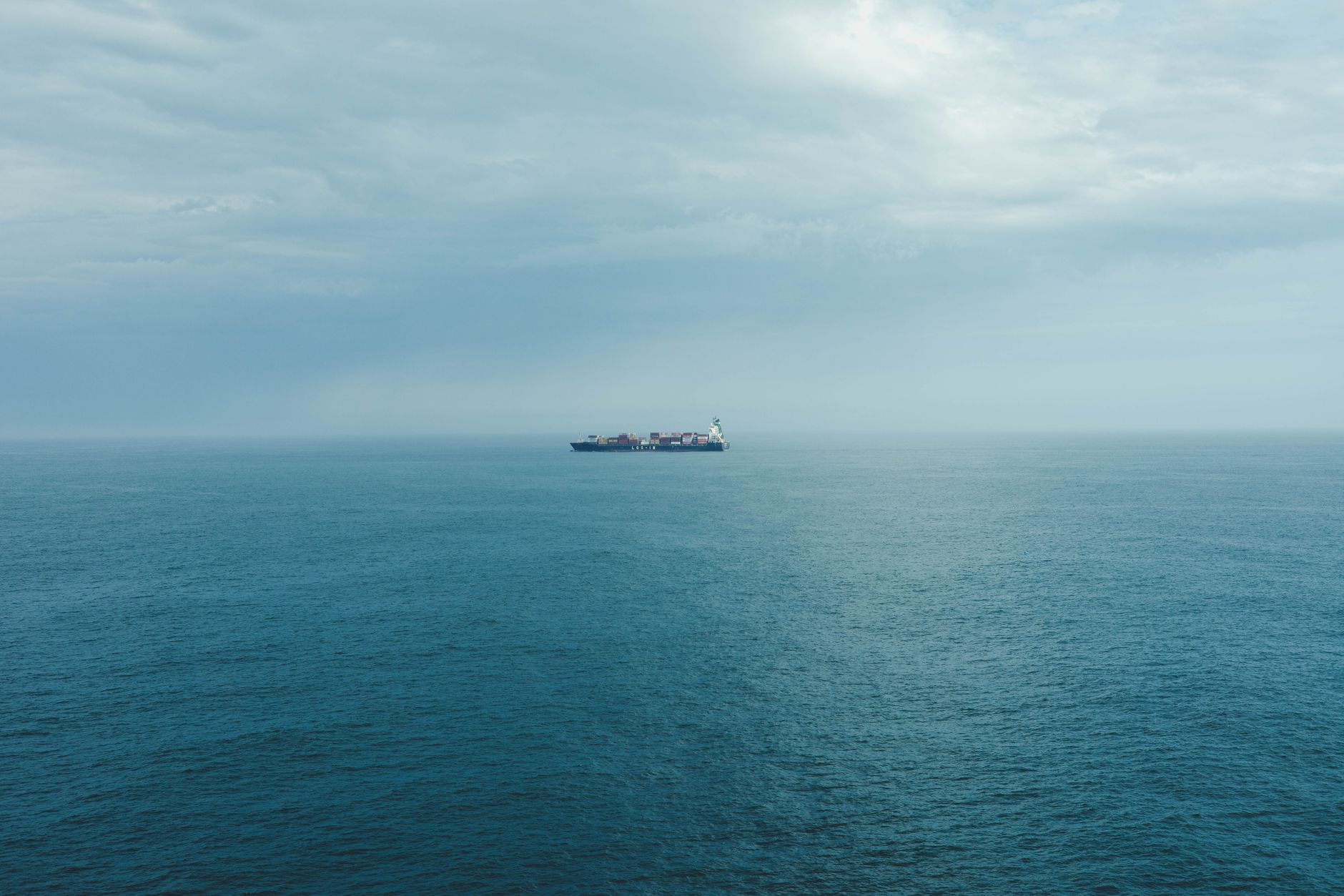 a carrier strike group formation at sea, with the supercarrier at center flanked by guided-missile destroyers and a cruiser visible on the horizon under partly cloudy skies