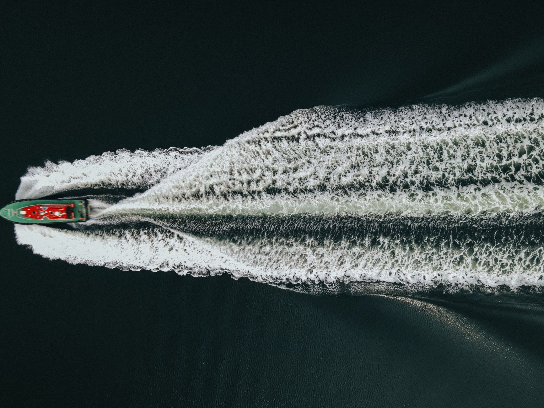 a naval destroyer underway at sea in open water, viewed from a low aerial angle with wake visible and no other vessels in frame