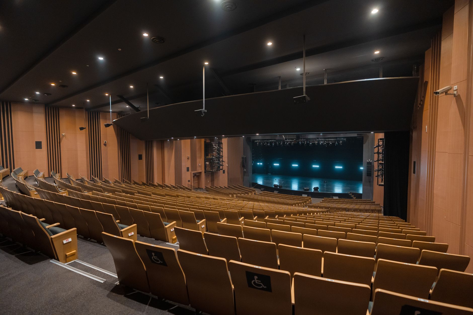 a large arena interior before a major live event, empty seats visible under dramatic stage lighting with a central performance stage and entrance ramp in the foreground