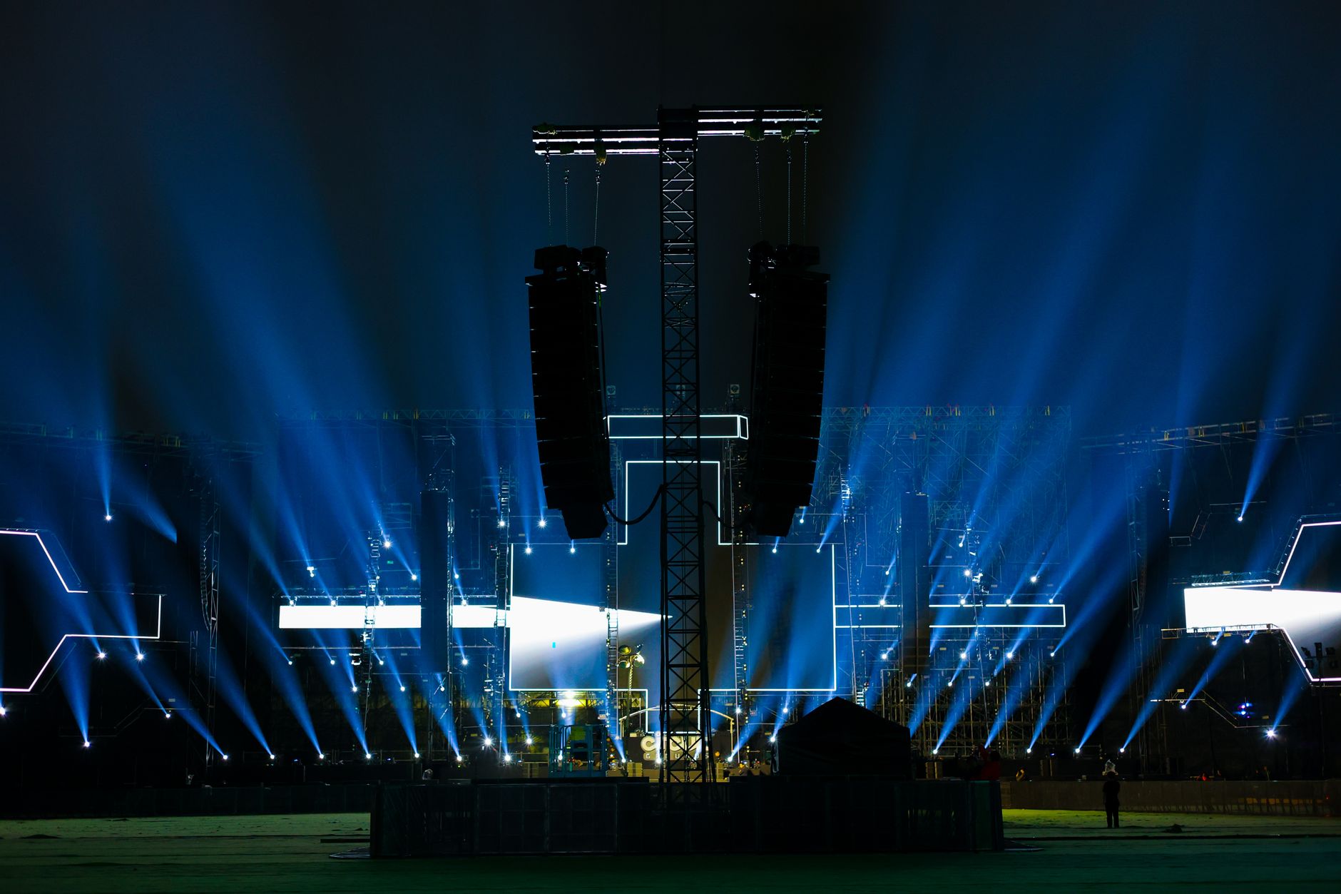 a large production truck and broadcast equipment staging area outside a major sports and entertainment venue, cables and antenna arrays visible along the exterior wall