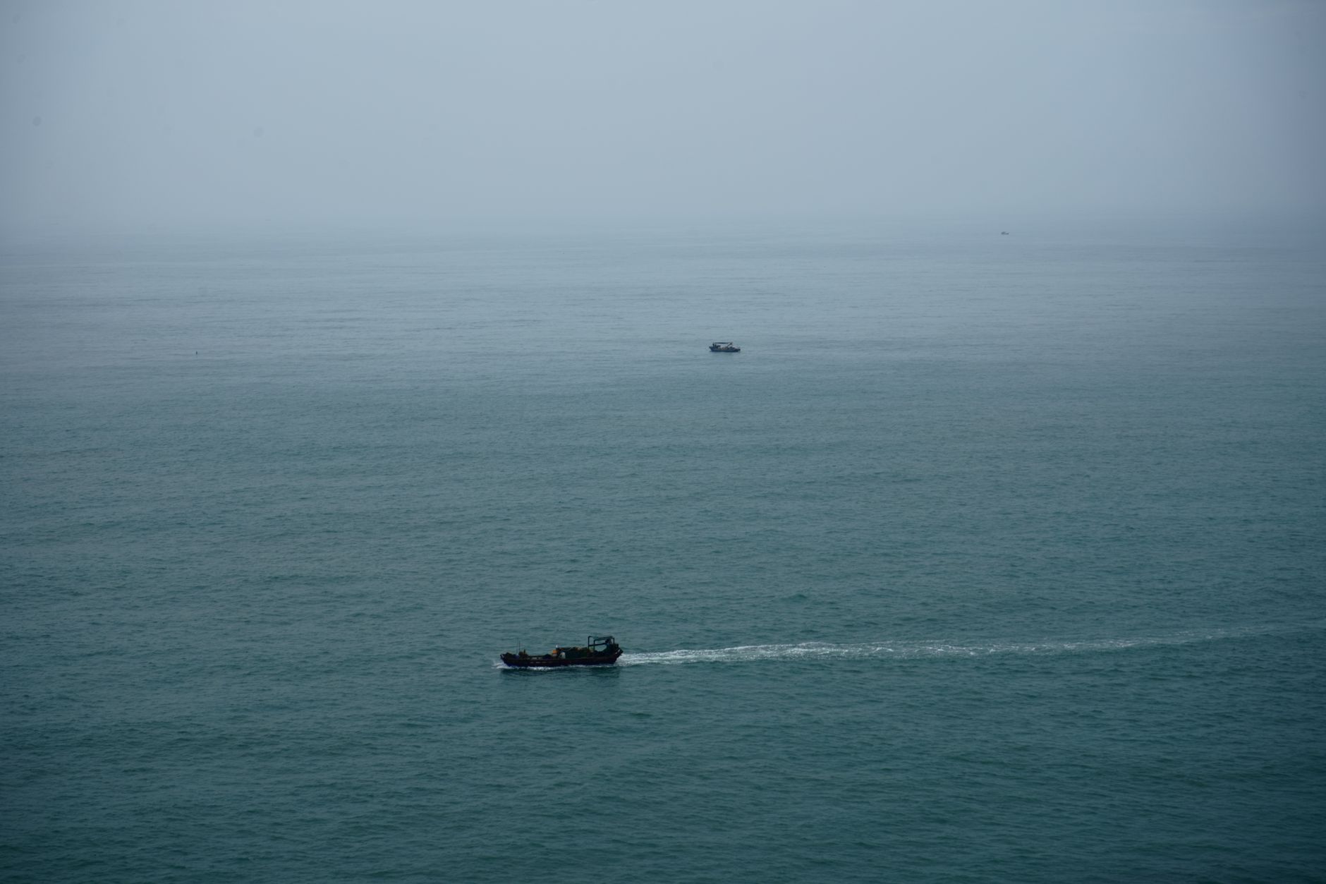 a Russian naval surface combatant at sea viewed from a wide angle, the vessel underway with visible forward deck launch systems against an overcast horizon