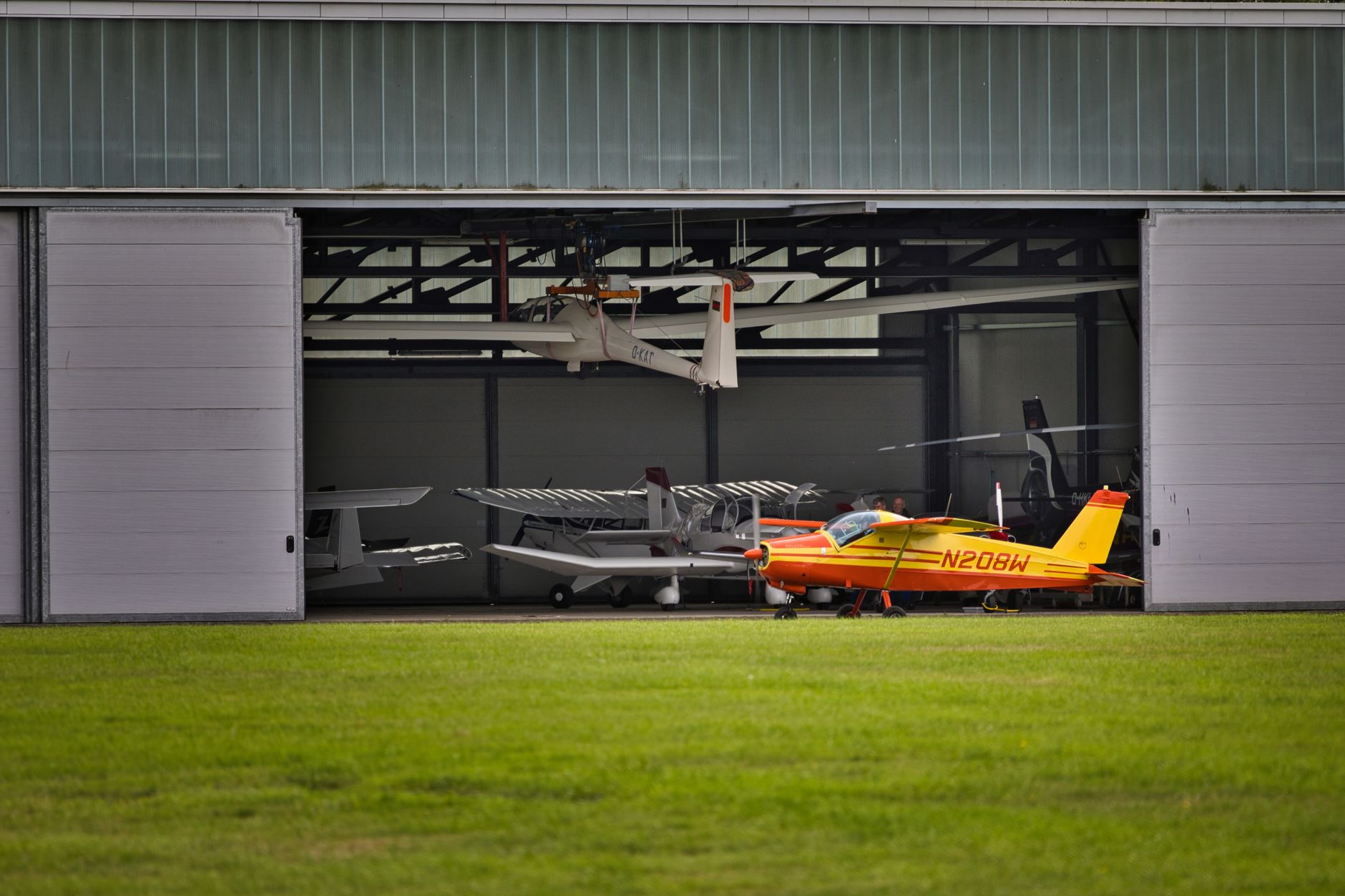 a military airfield flight line with unmanned aircraft parked in a row inside an open hangar, ground support equipment visible nearby