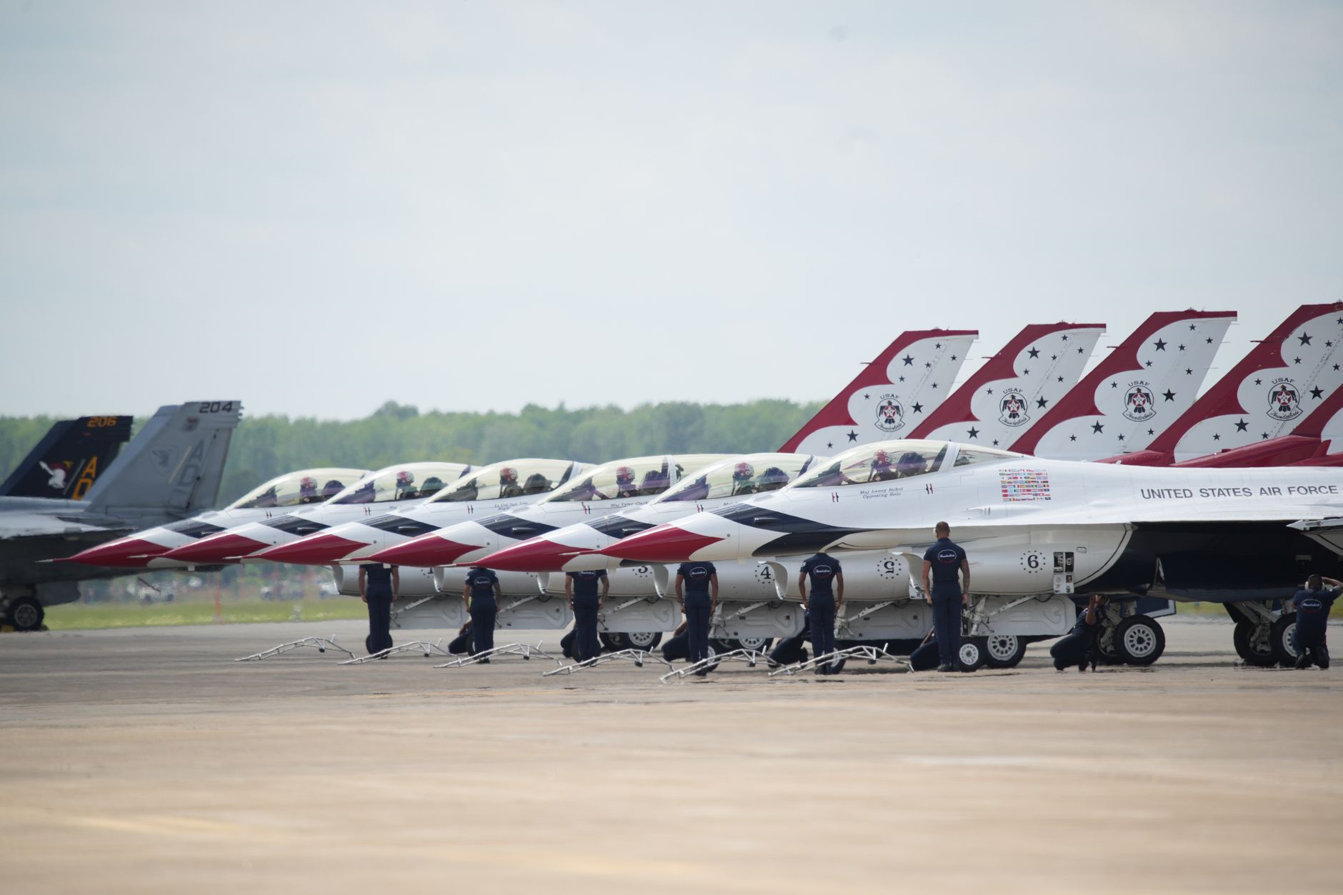 rows of F-35A and F-16 fighter jets parked on a wide flight line at a major Air Force base, viewed from an elevated angle in daylight