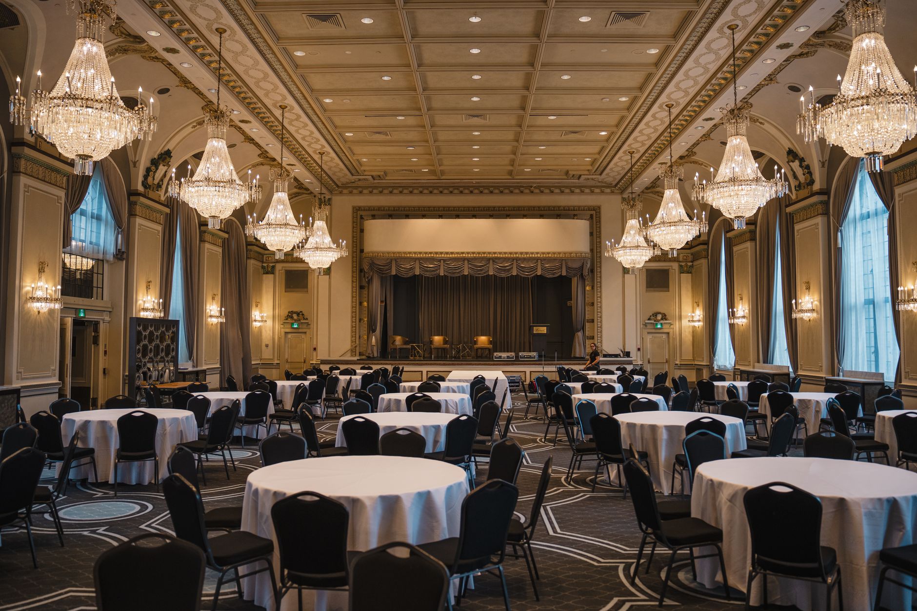 wide interior shot of a large convention center ballroom configured for a military leadership conference, rows of chairs facing a large projection screen, no people as focal point