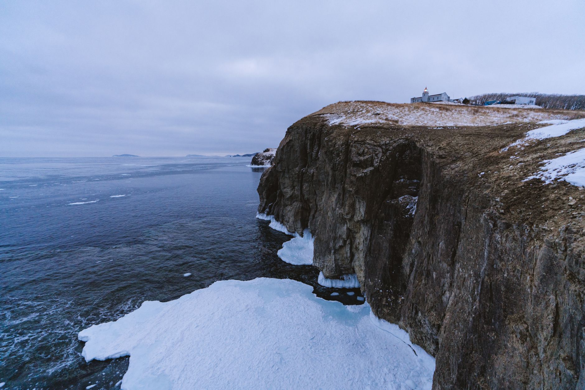 a partially frozen Arctic coastline with a distant radar installation and communication towers visible against a low winter sky, no people in frame