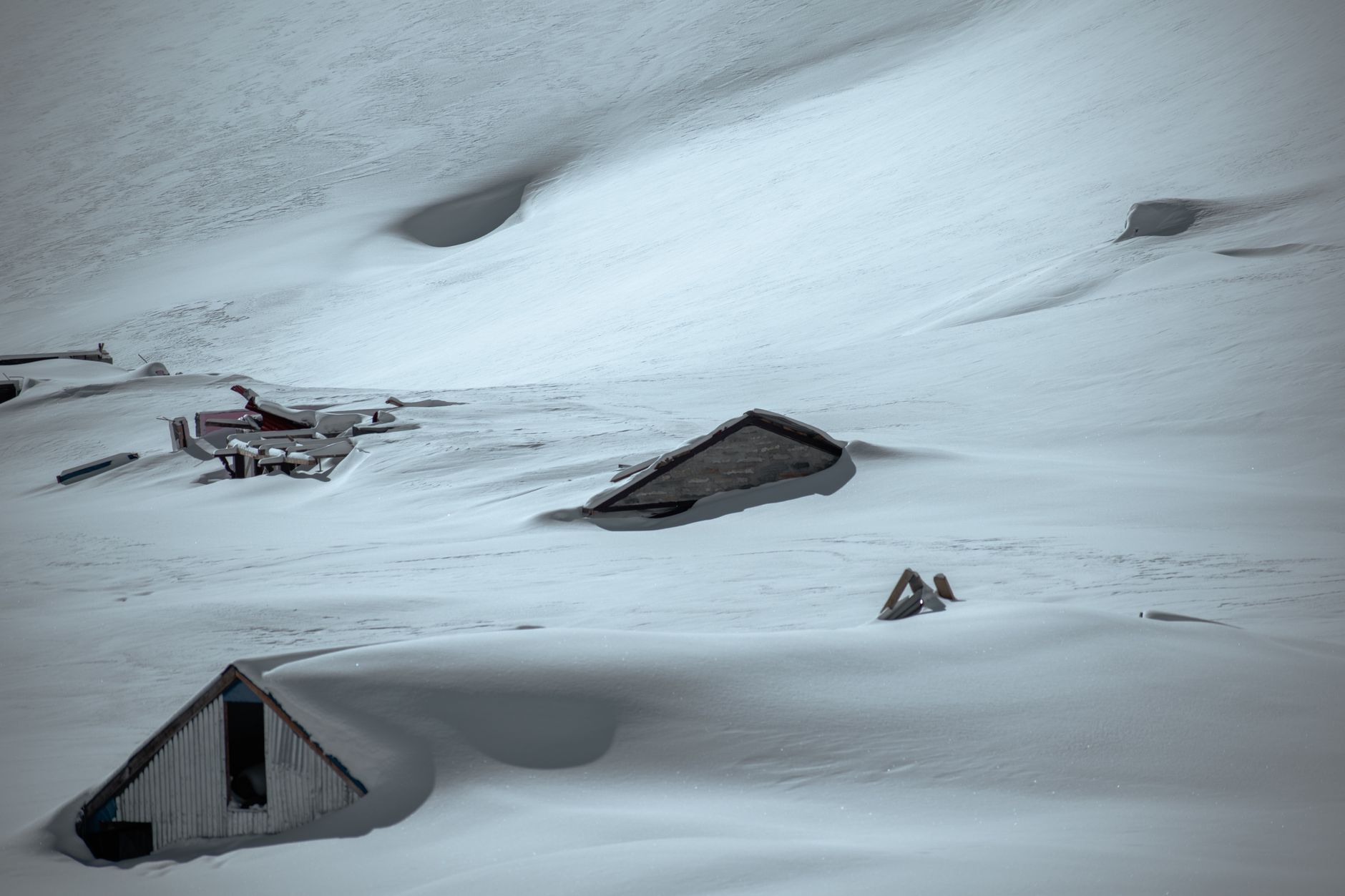 A cold-weather military field shelter partially buried in snow on an Arctic plateau, with communication antennas extending from the structure