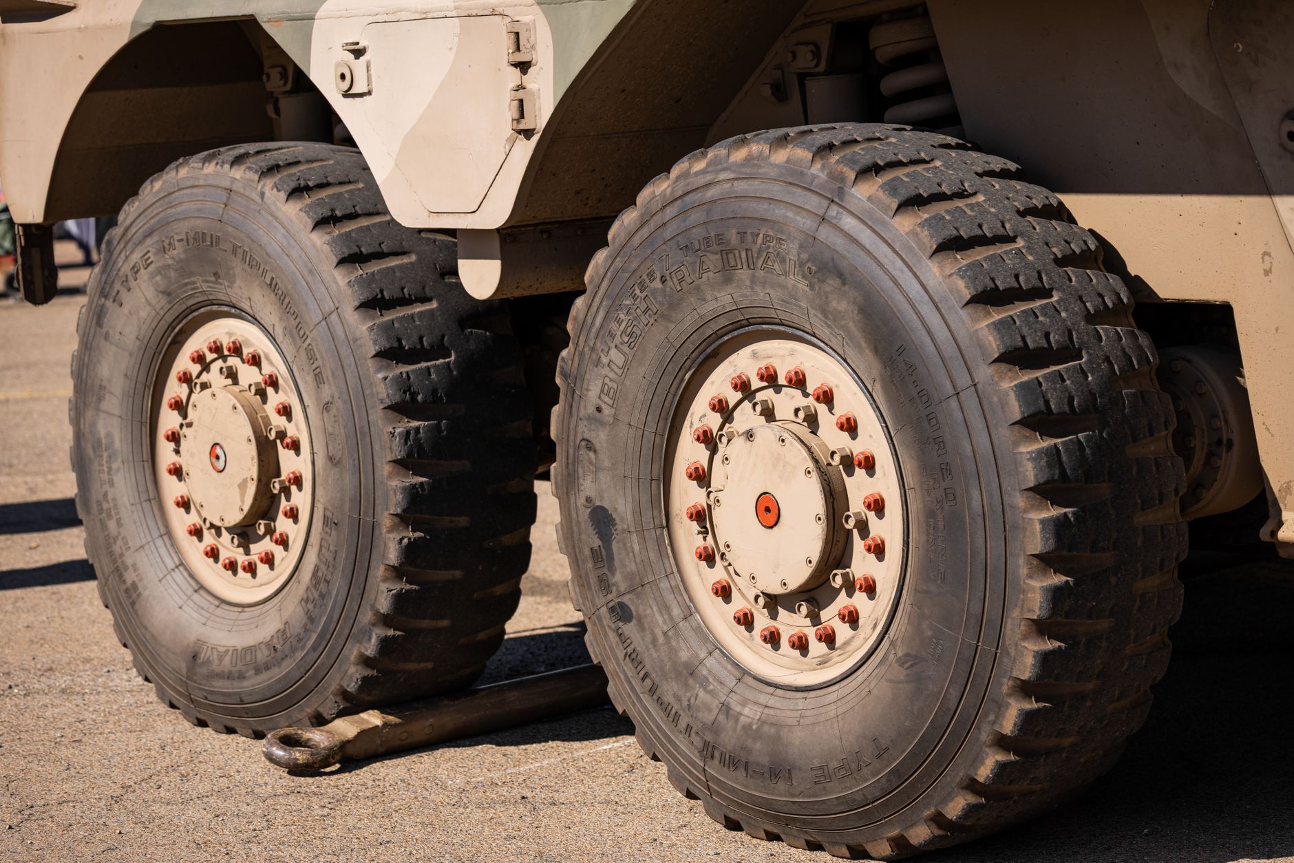 a military ground vehicle equipped with sensor mast and antenna arrays in an open-air testing environment, surrounded by sparse terrain