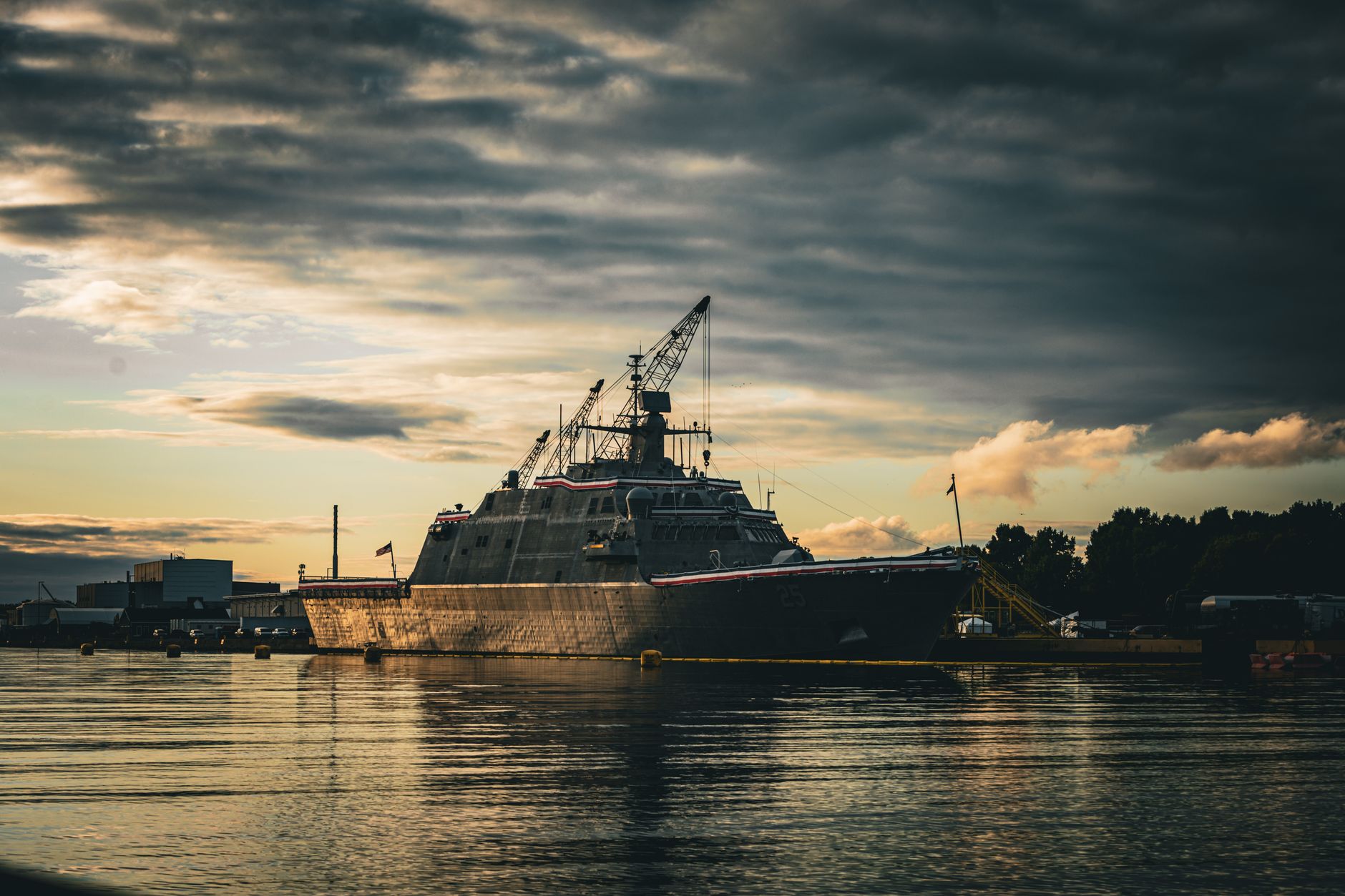 A naval support vessel moored at a European port with unmanned surface vehicles secured on its rear deck, calm harbor water visible in the foreground