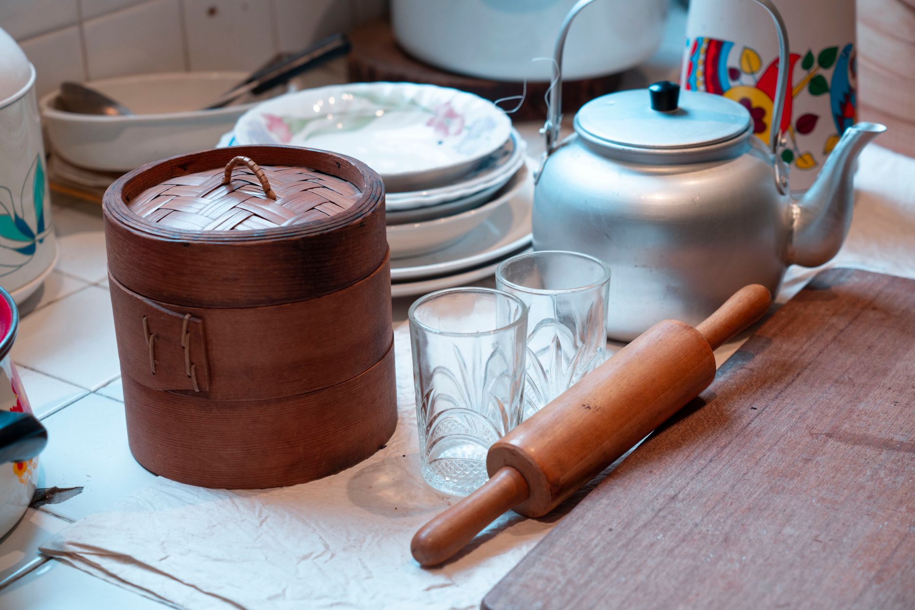 a sparse, well-lit living room styled in a mid-century domestic aesthetic, with baking tools arranged neatly on a kitchen counter visible in the background, no people as the focal subject