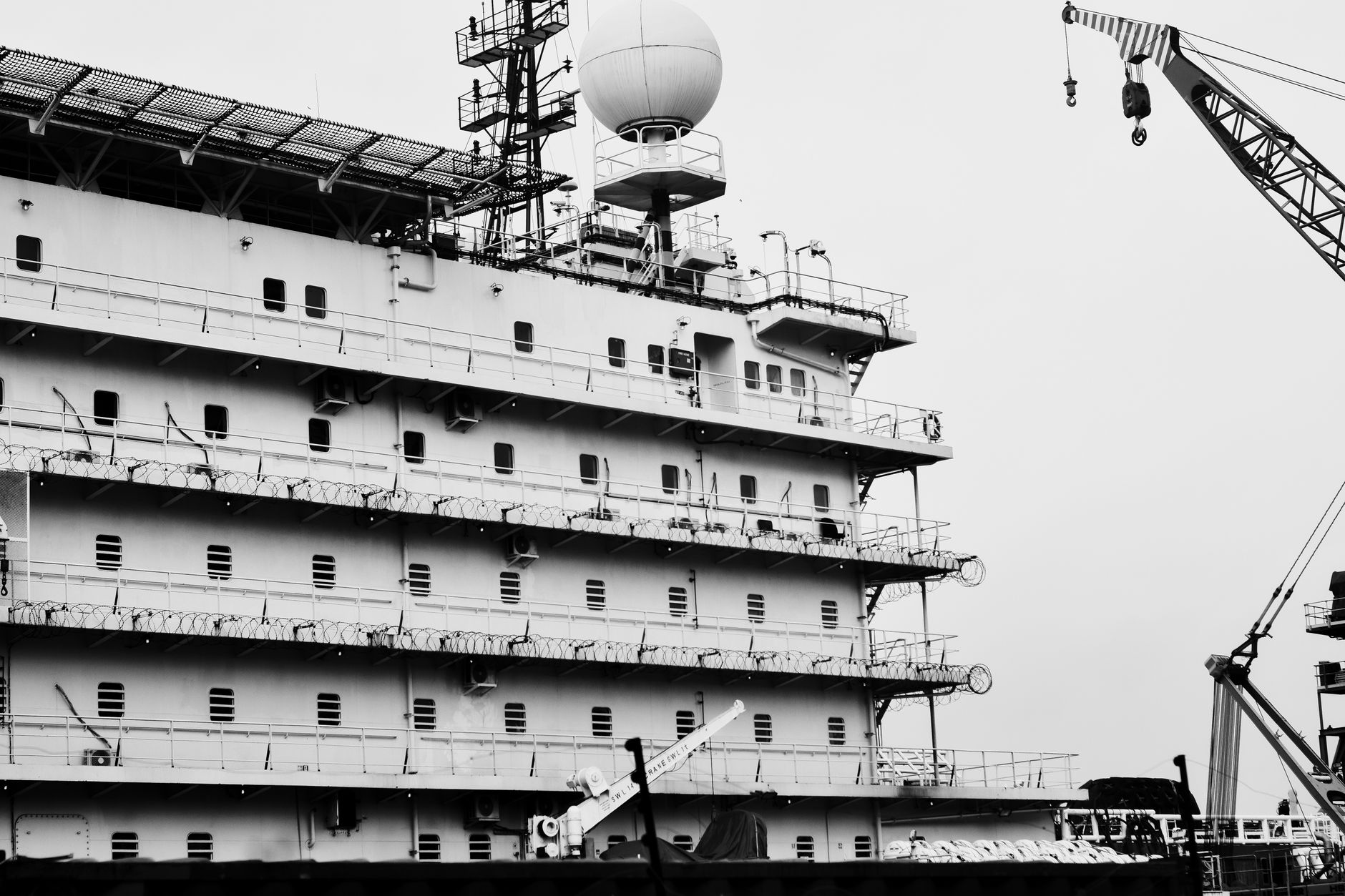 A large gray naval auxiliary vessel under construction in a covered dry dock, viewed from above, with cranes and scaffolding visible along the hull