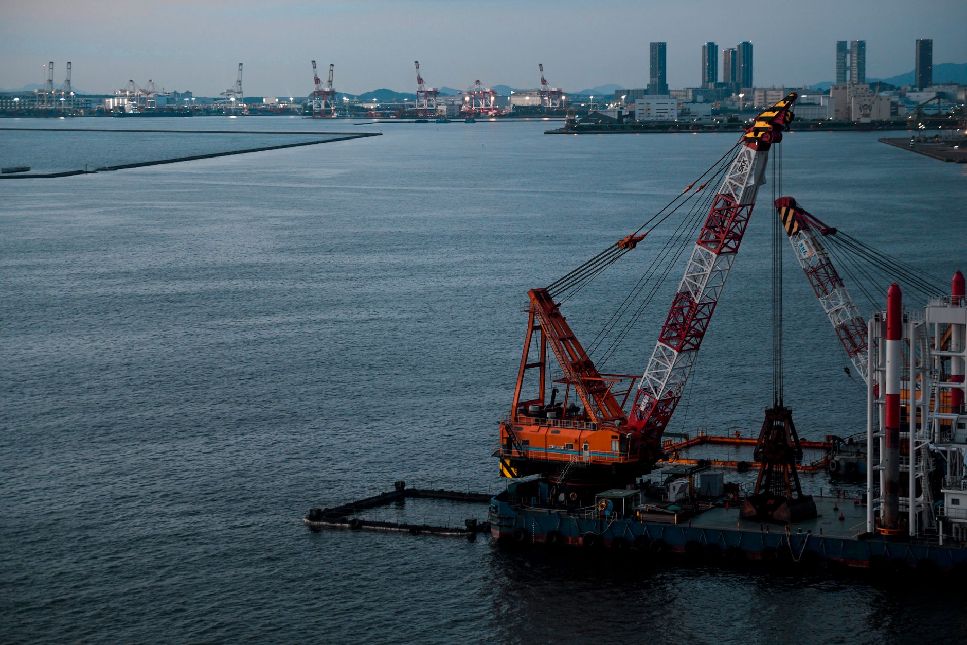 Wide aerial view of a Chinese commercial shipyard showing multiple dry docks, gantry cranes, and partially constructed gray hulls alongside a waterway