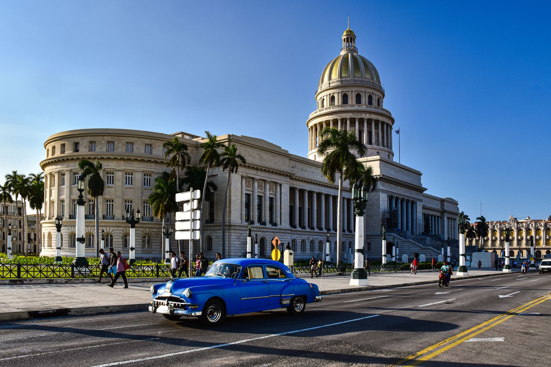 wide-angle view of a weathered, paint-stripped Havana streetscape with vintage American automobiles parked along a cracked colonial-era boulevard, no people as focal point