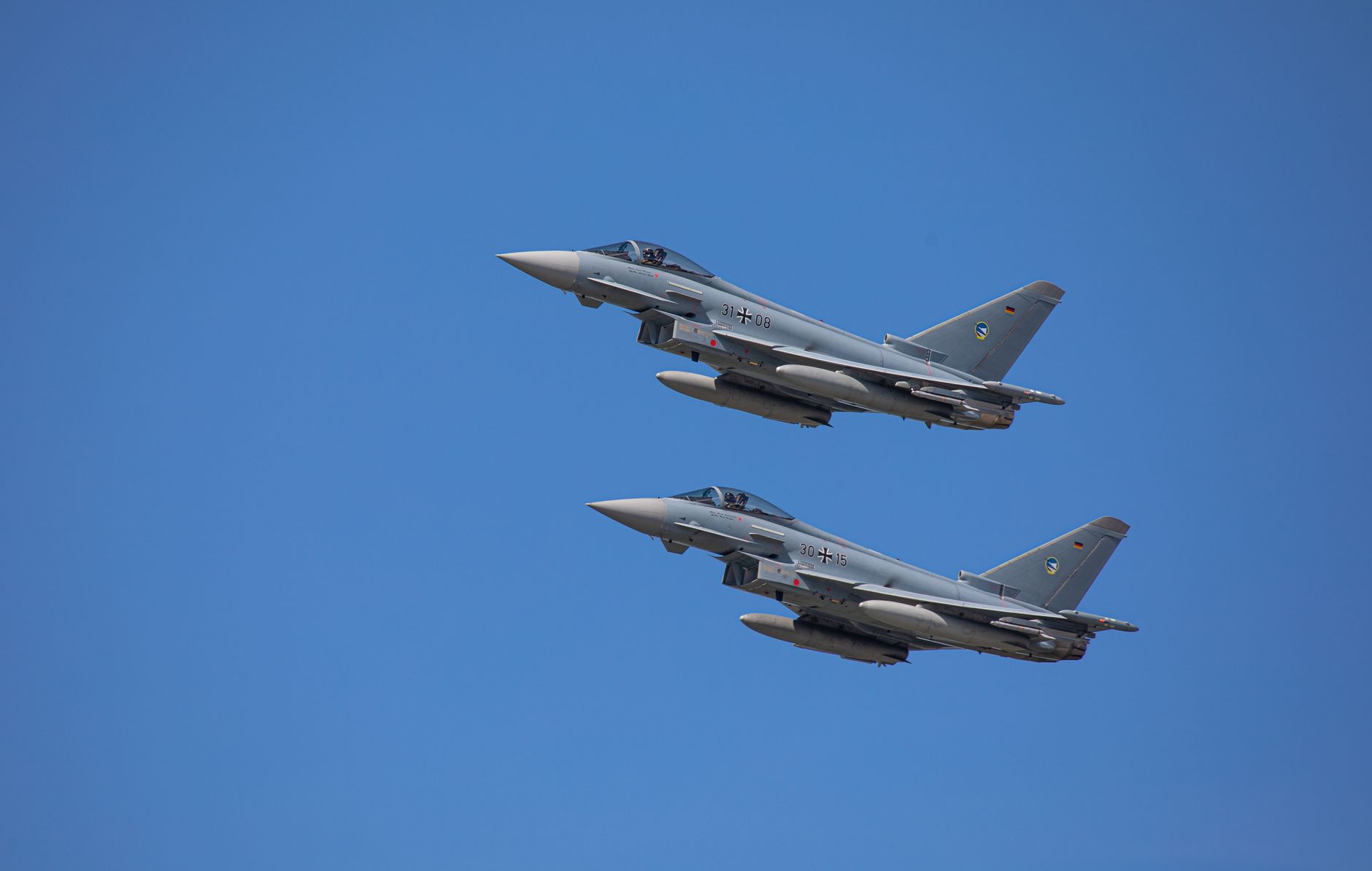 a Eurofighter Typhoon jet parked on a flight line at a European air base, engines visible from the rear, ground support equipment staged nearby