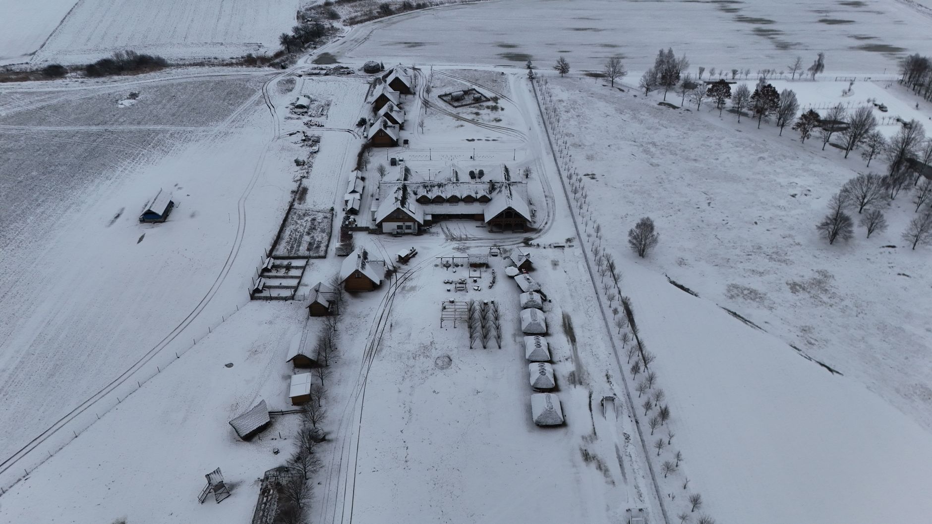 a long row of battle tanks parked on a snow-dusted European military base tarmac, viewed from an elevated angle with maintenance crews working in the distance