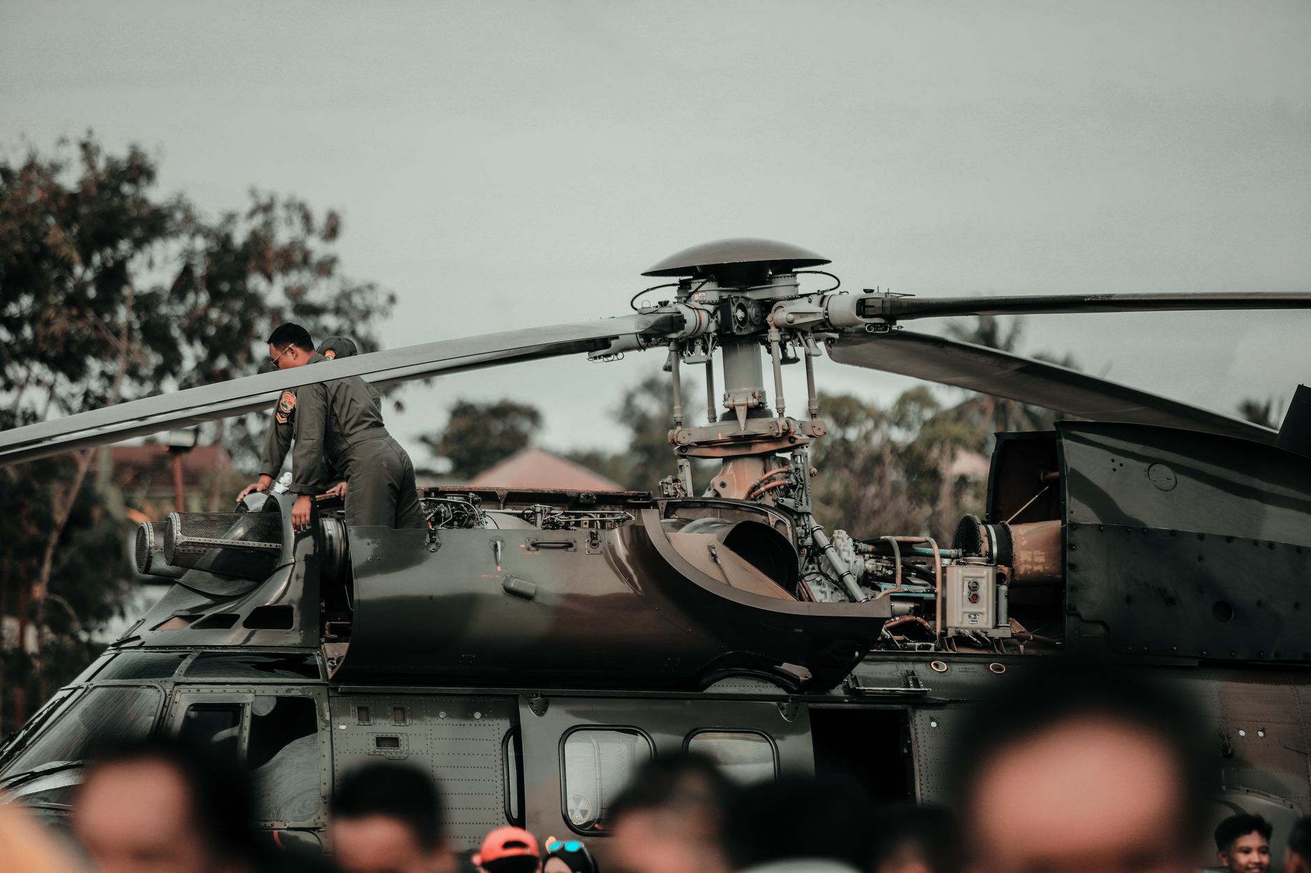 a compact, open-frame light tactical vehicle with roll cage and modular weapon mount station positioned on a tarmac apron near a military transport helicopter