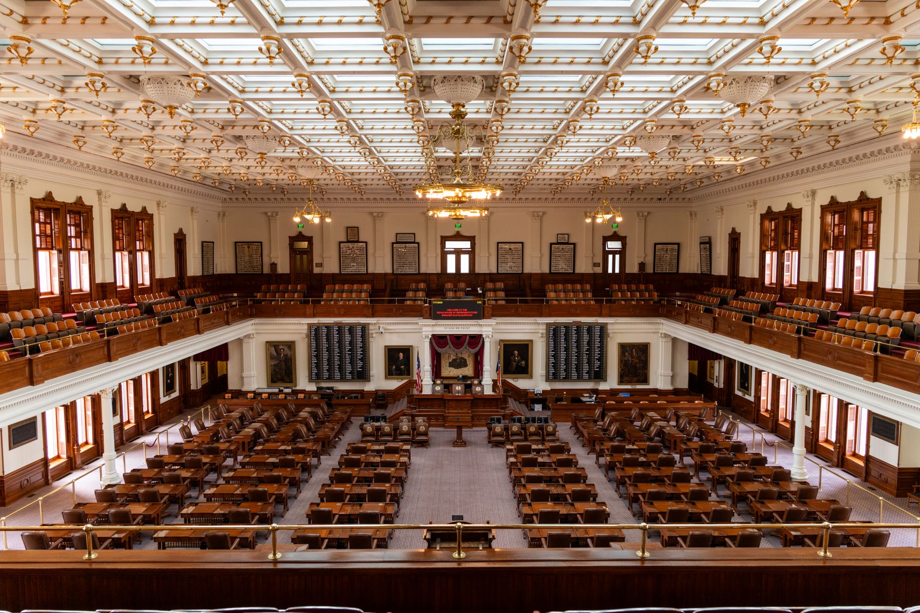 a congressional hearing room viewed from the gallery level, rows of empty chairs at a curved dais under fluorescent lighting, no people present