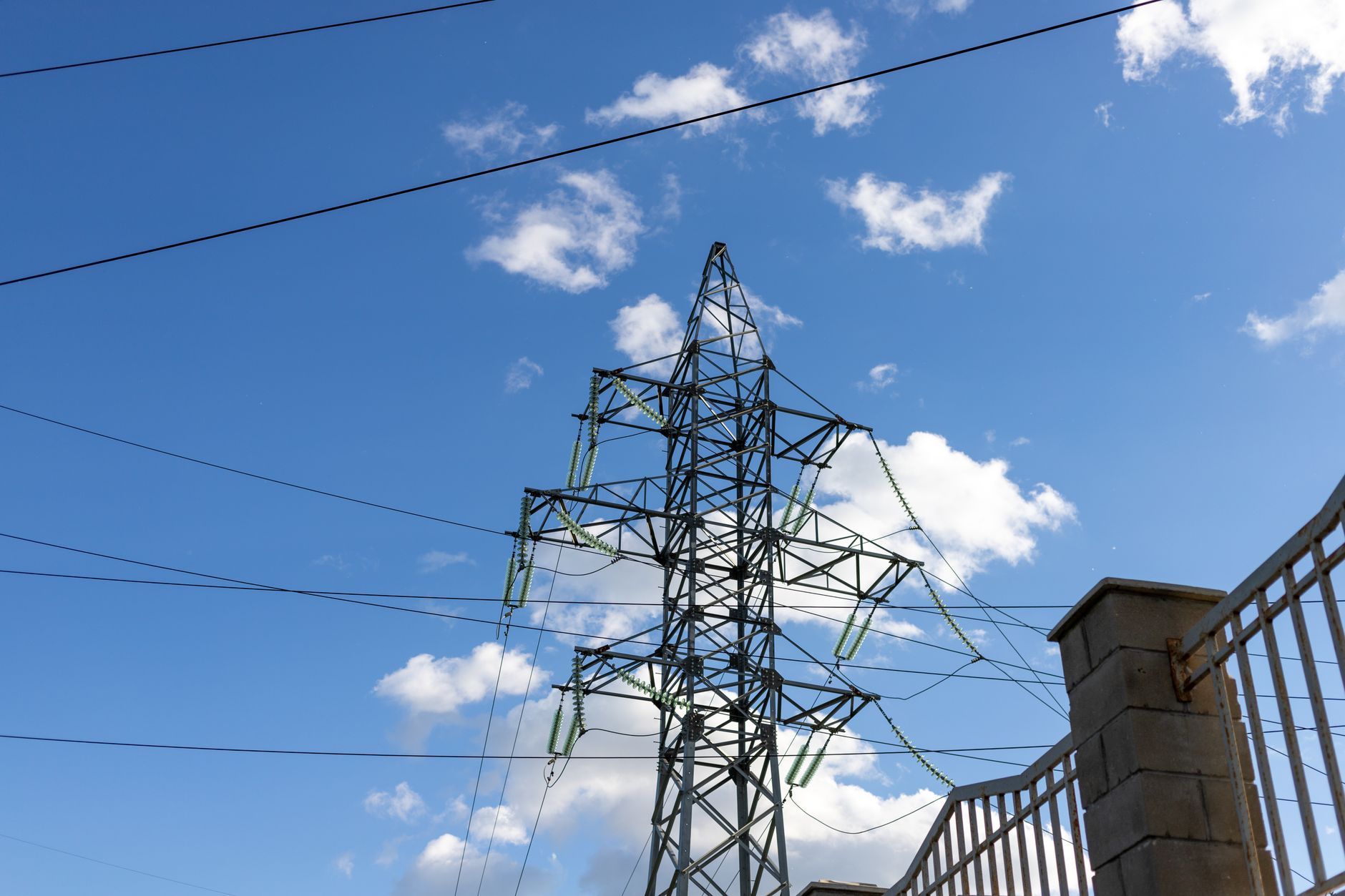 a high-voltage electrical transmission substation with large transformers and steel lattice towers, surrounded by security fencing, overcast sky