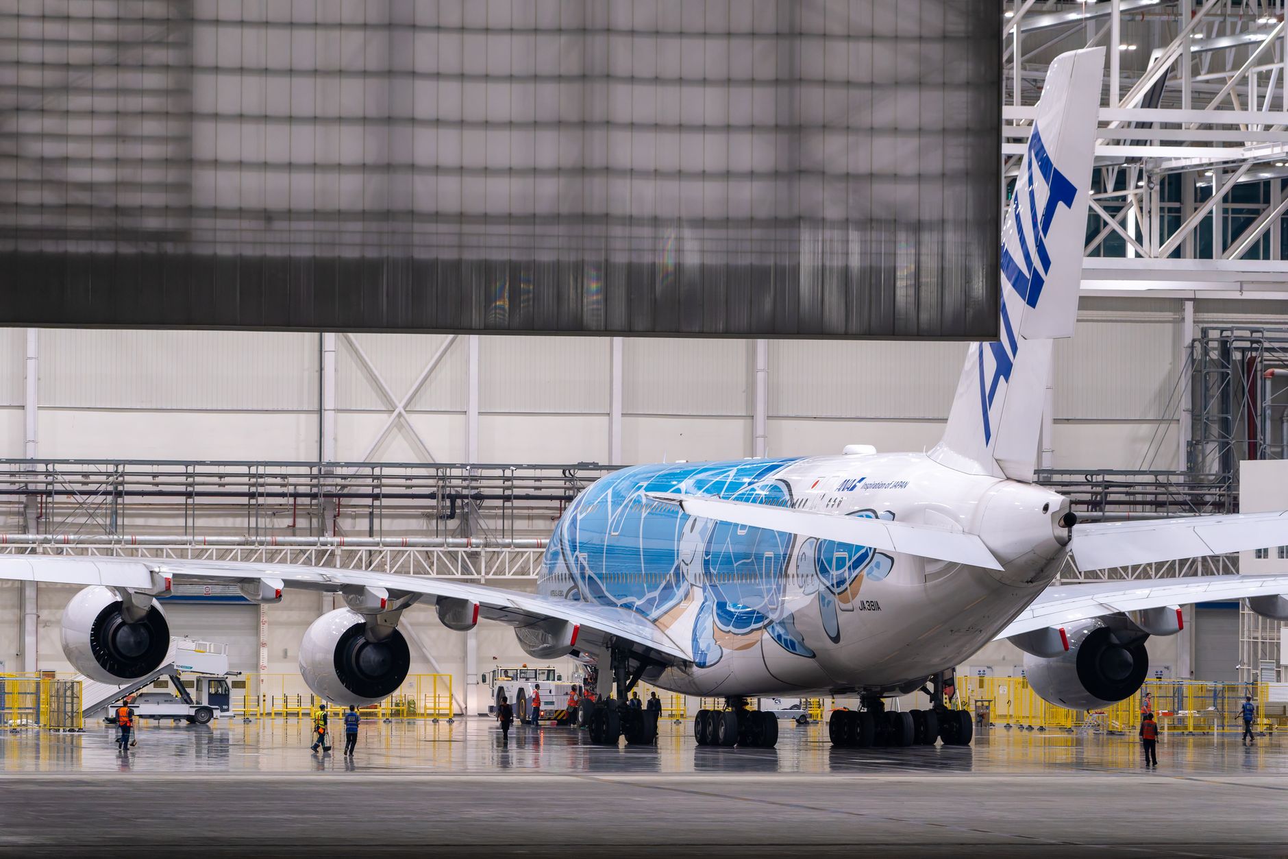 a wide-body Airbus A330 aircraft in a large maintenance hangar with its cargo door open during a conversion modification process, scaffolding visible along the fuselage