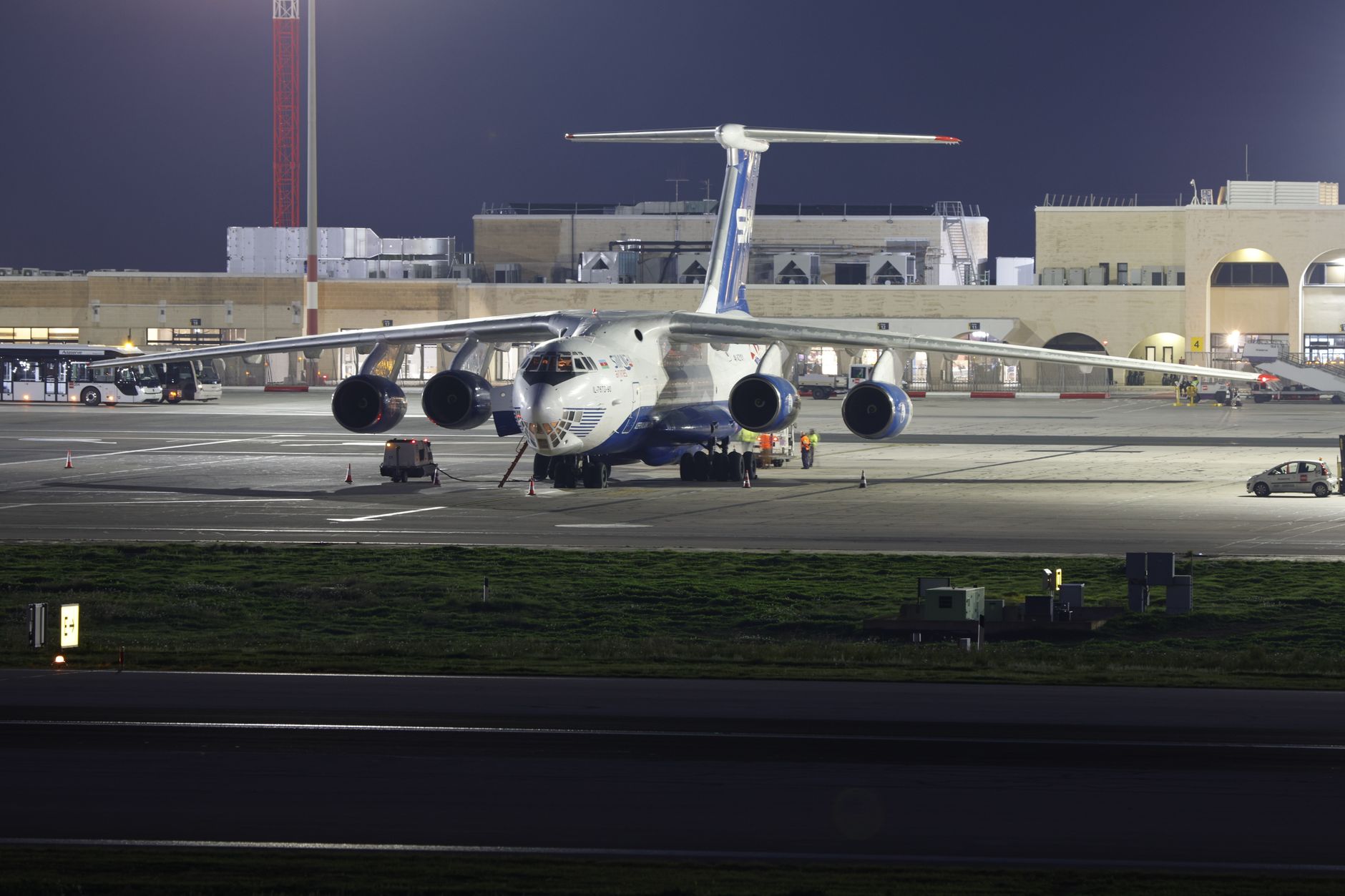 rows of converted freighter aircraft parked on an airport apron at dusk, cargo containers visible on ground-handling equipment nearby