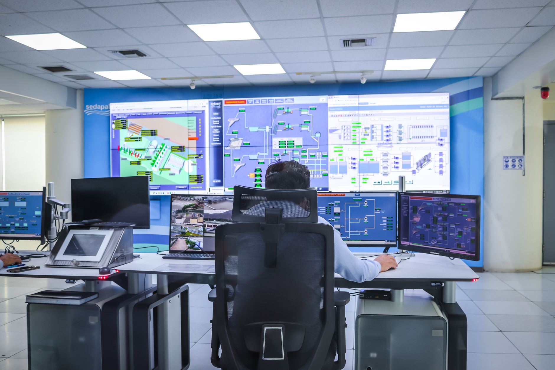 a command and control operations center with large digital displays showing real-time data overlays, unmanned system feeds, and situational awareness grids, viewed from a wide angle showing the room's full layout