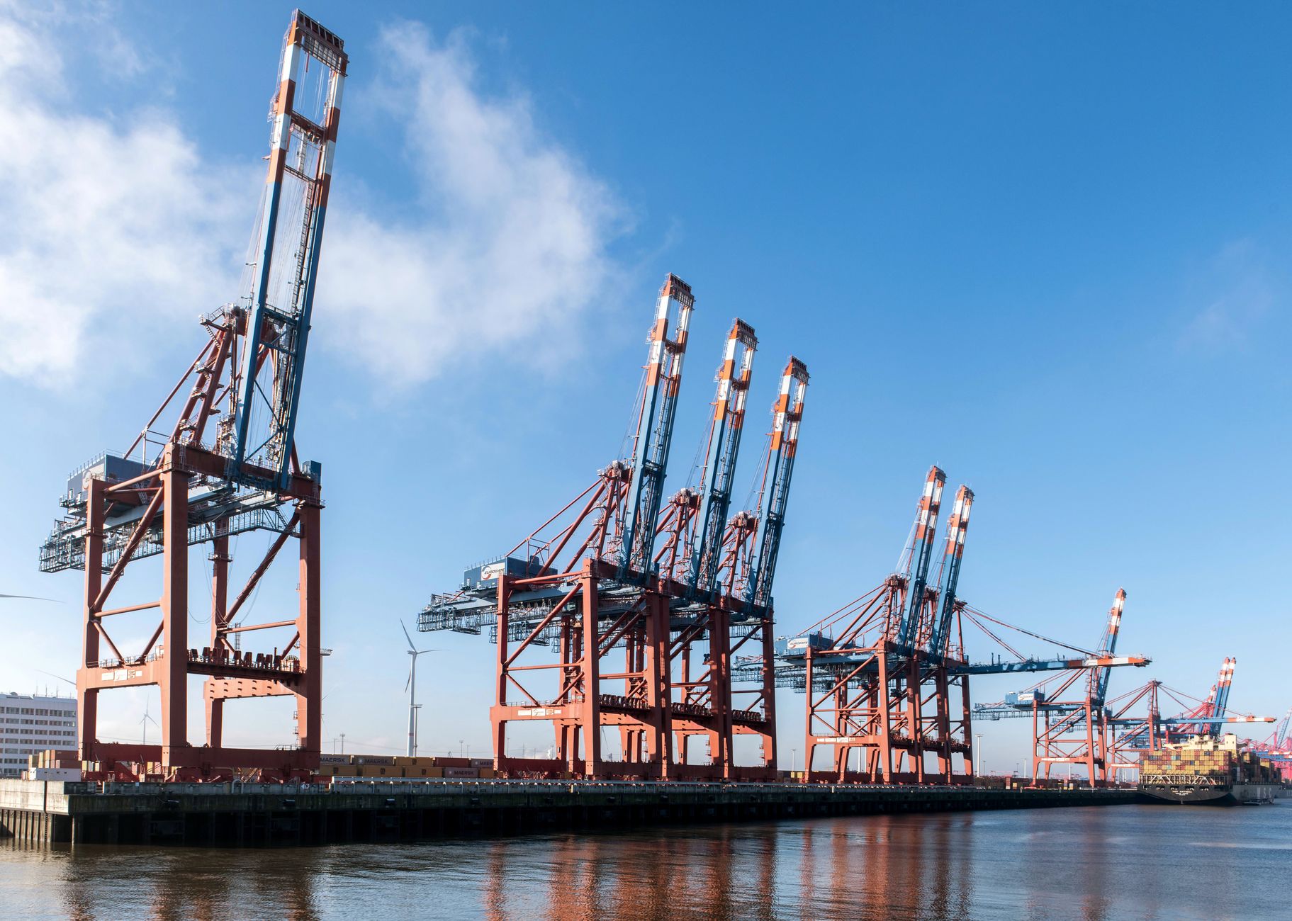 a commercial cargo terminal with shipping containers and freight handling equipment under overcast skies, viewed from a wide angle showing the dock infrastructure