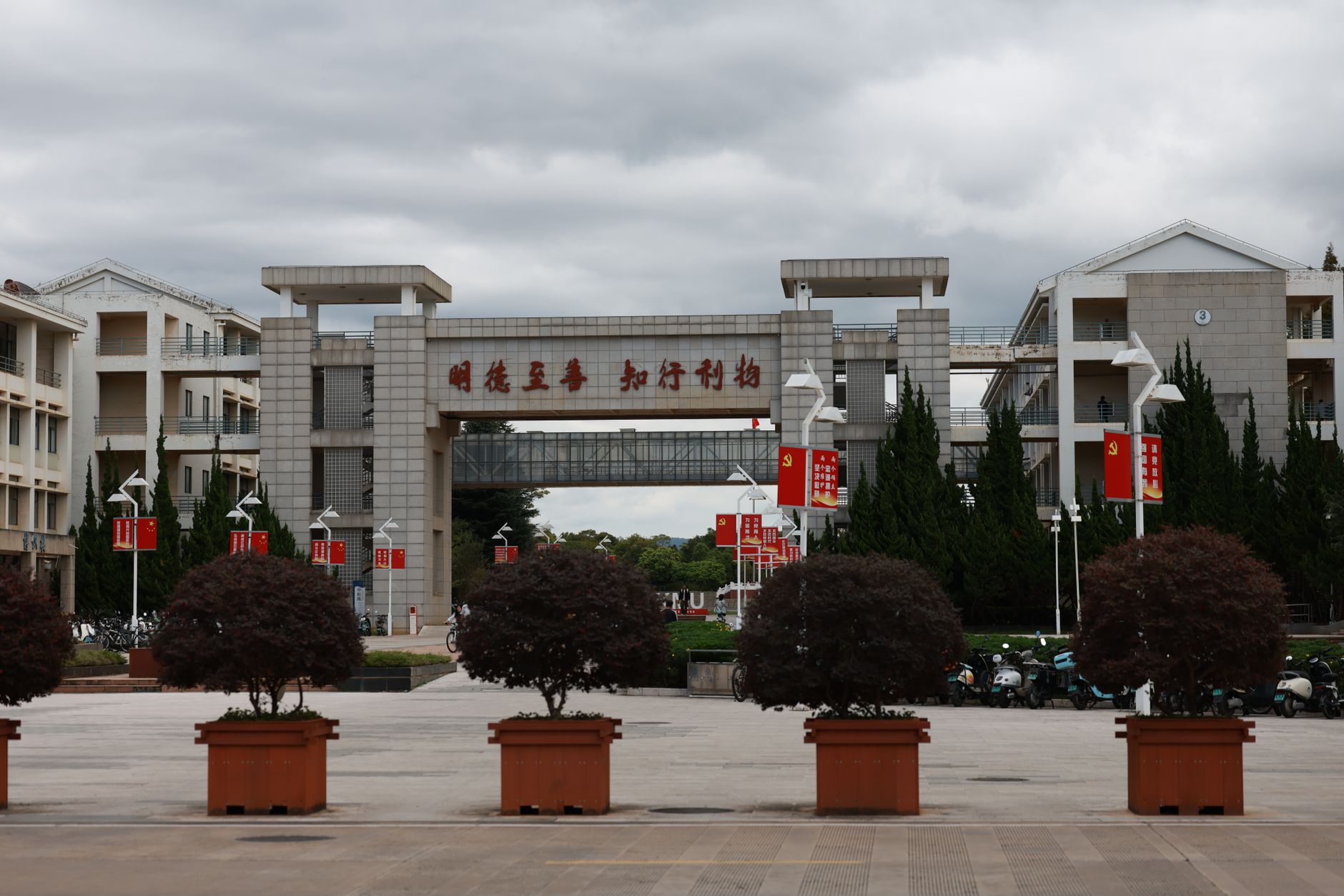 a modern university campus building exterior with a wide stone plaza and rows of empty benches in early morning light