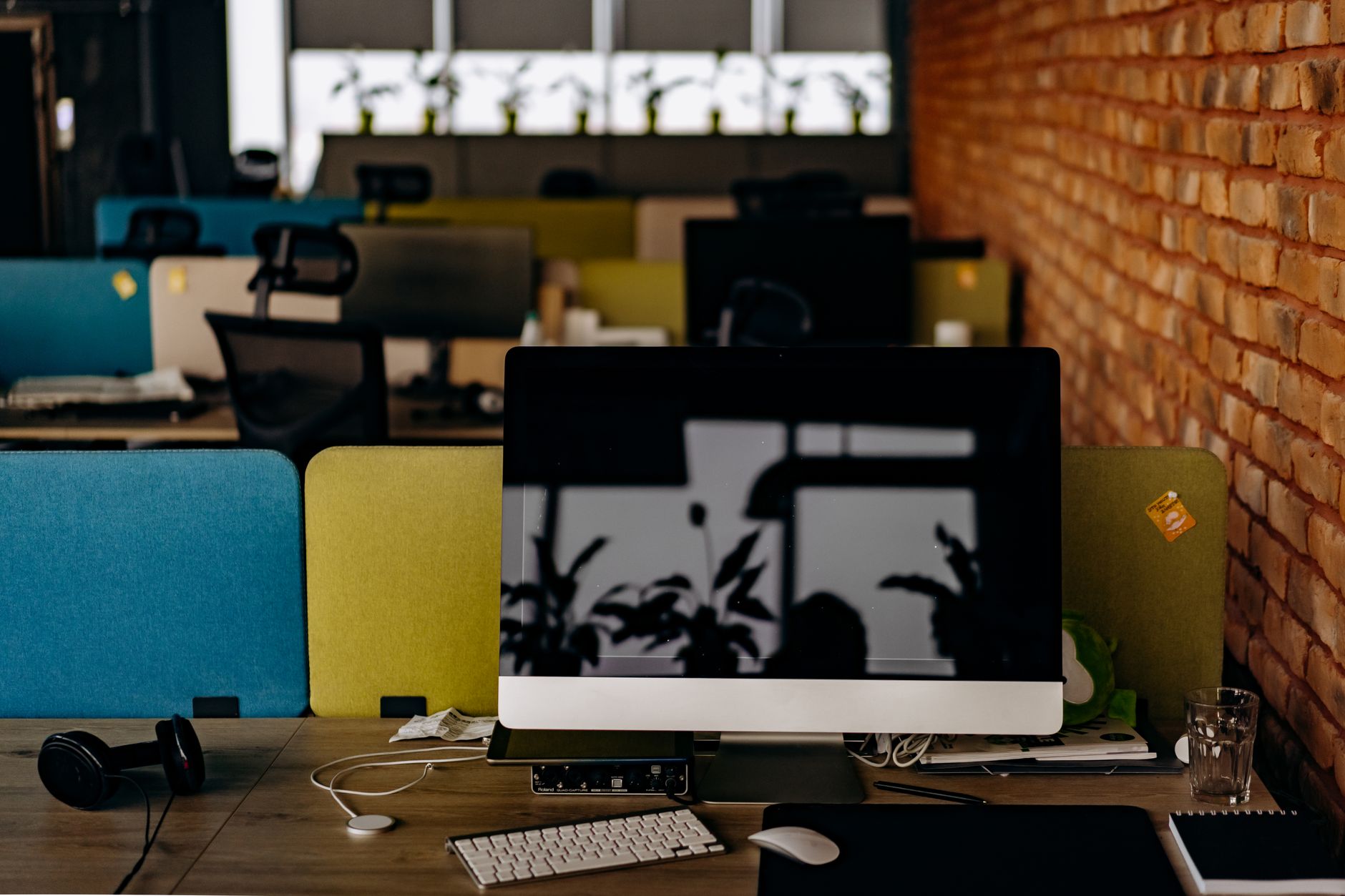rows of desktop workstations in an empty open-plan office with natural light coming through floor-to-ceiling windows, chairs pushed in and screens dark