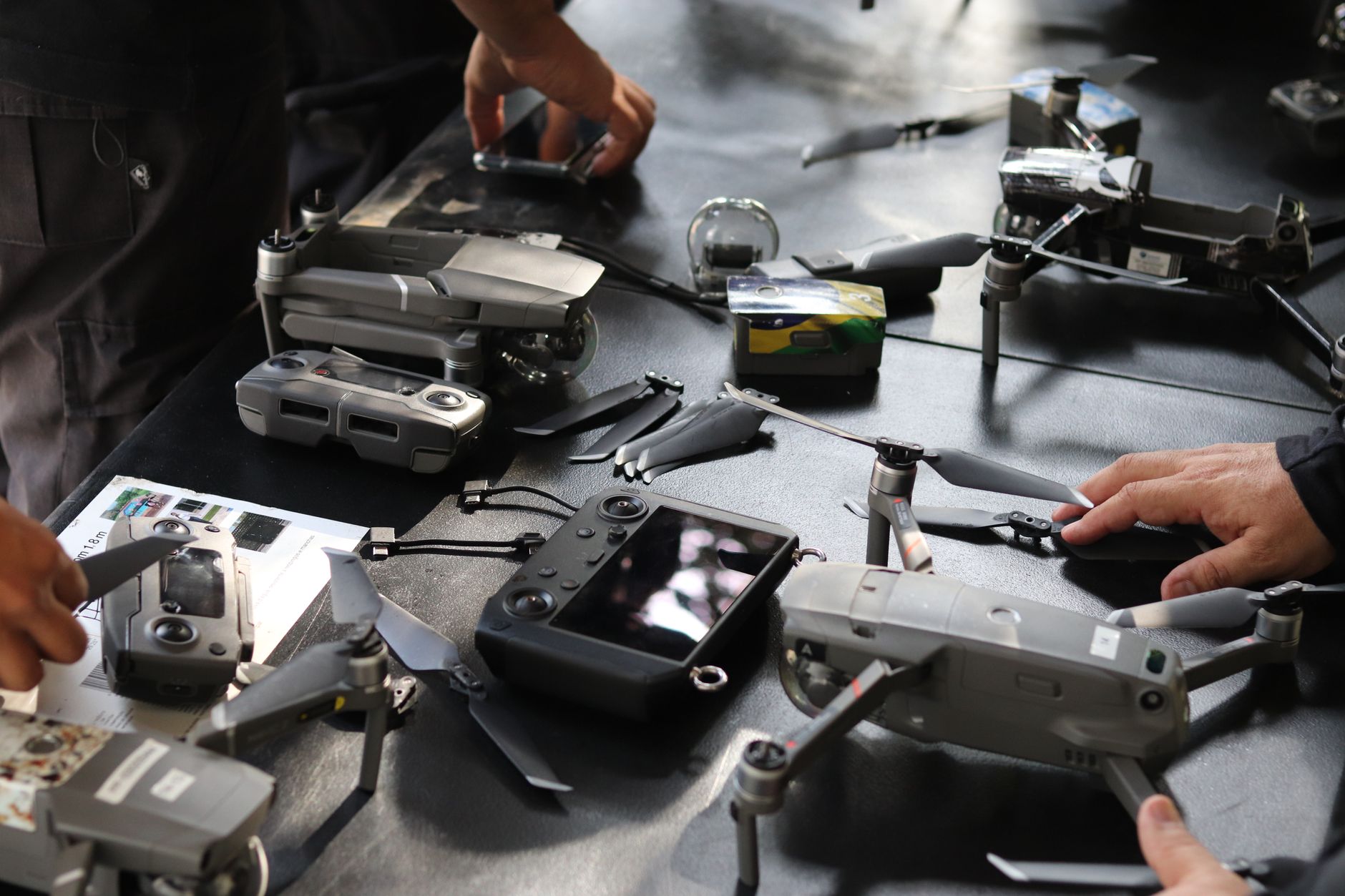 a military technology exhibition floor displaying rows of small tactical unmanned ground vehicles and quadcopter drones on display stands inside a large indoor facility