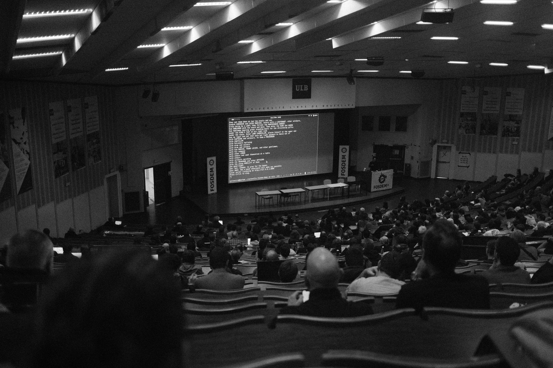 a venture capital pitch event inside a minimalist conference center, with a projected slide visible on a large screen and rows of chairs facing a presentation podium, no people as focal subject